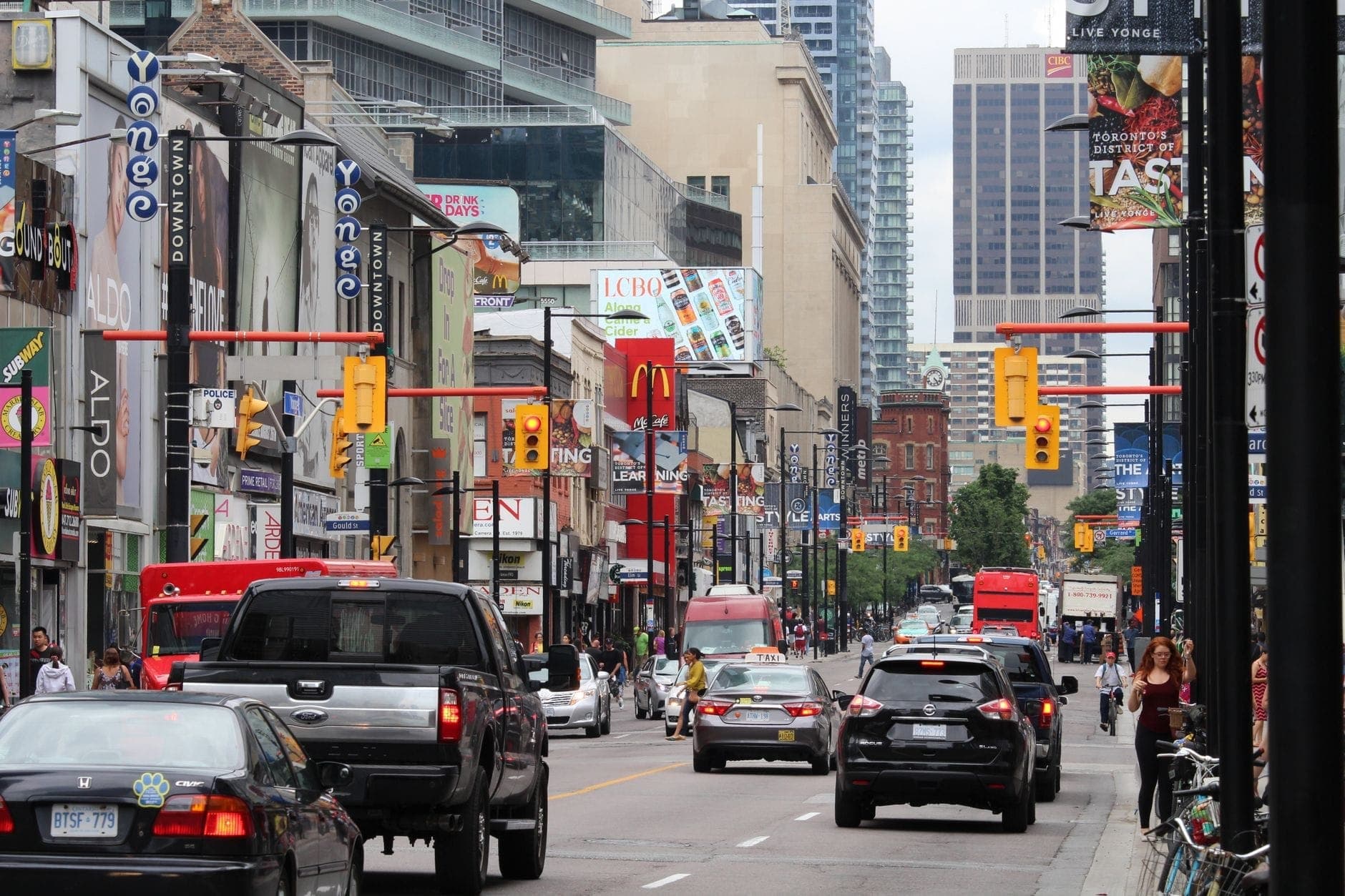 Busy street view of Yonge Street in downtown Toronto with cars, shops, signs, and people on the sidewalks.