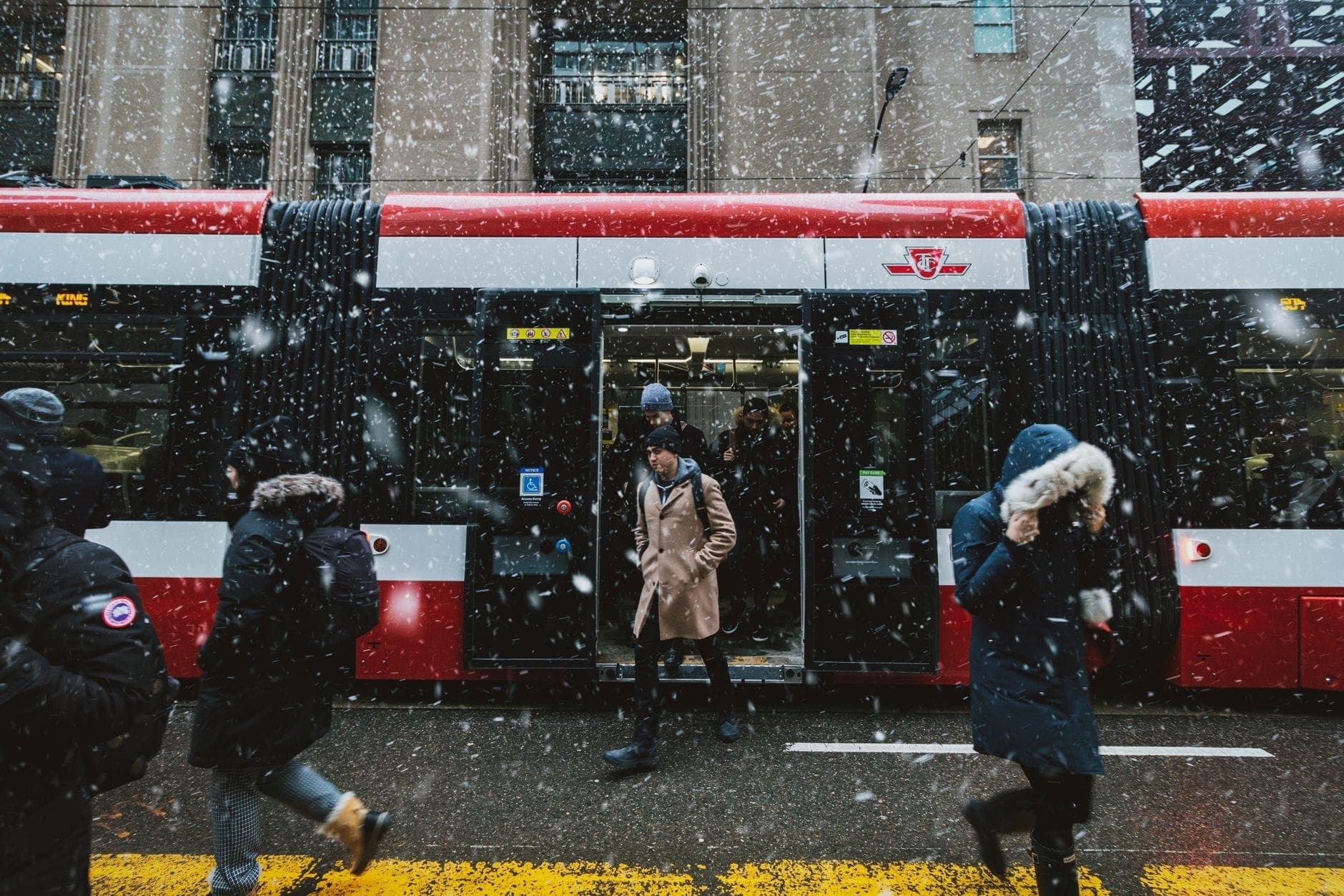 People exiting and boarding a TTC streetcar in downtown Toronto during snowfall, with clear red and white transit colors.