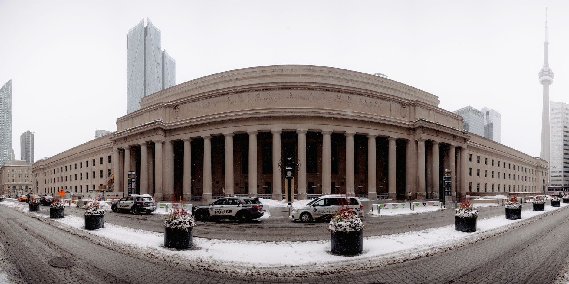 Wide angle view of Toronto's Union Station exterior in winter, showing its grand columns, snow on the ground, and nearby CN Tower.