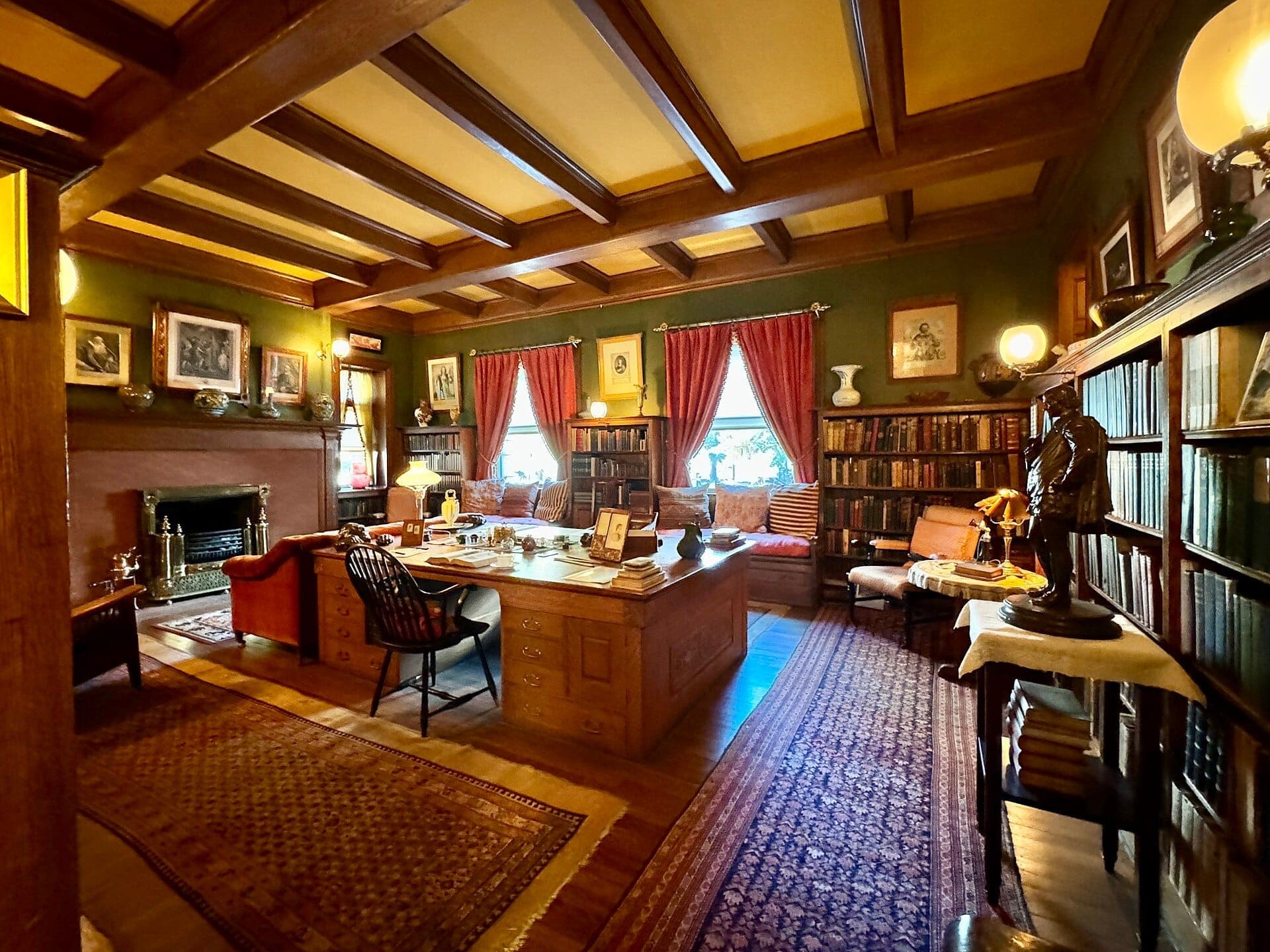 Sala de estudio histórica en el Glessner House Museum con techo de vigas de madera, escritorio antiguo, chimenea, estanterías, arte enmarcado y ventanas con cortinas rojas.