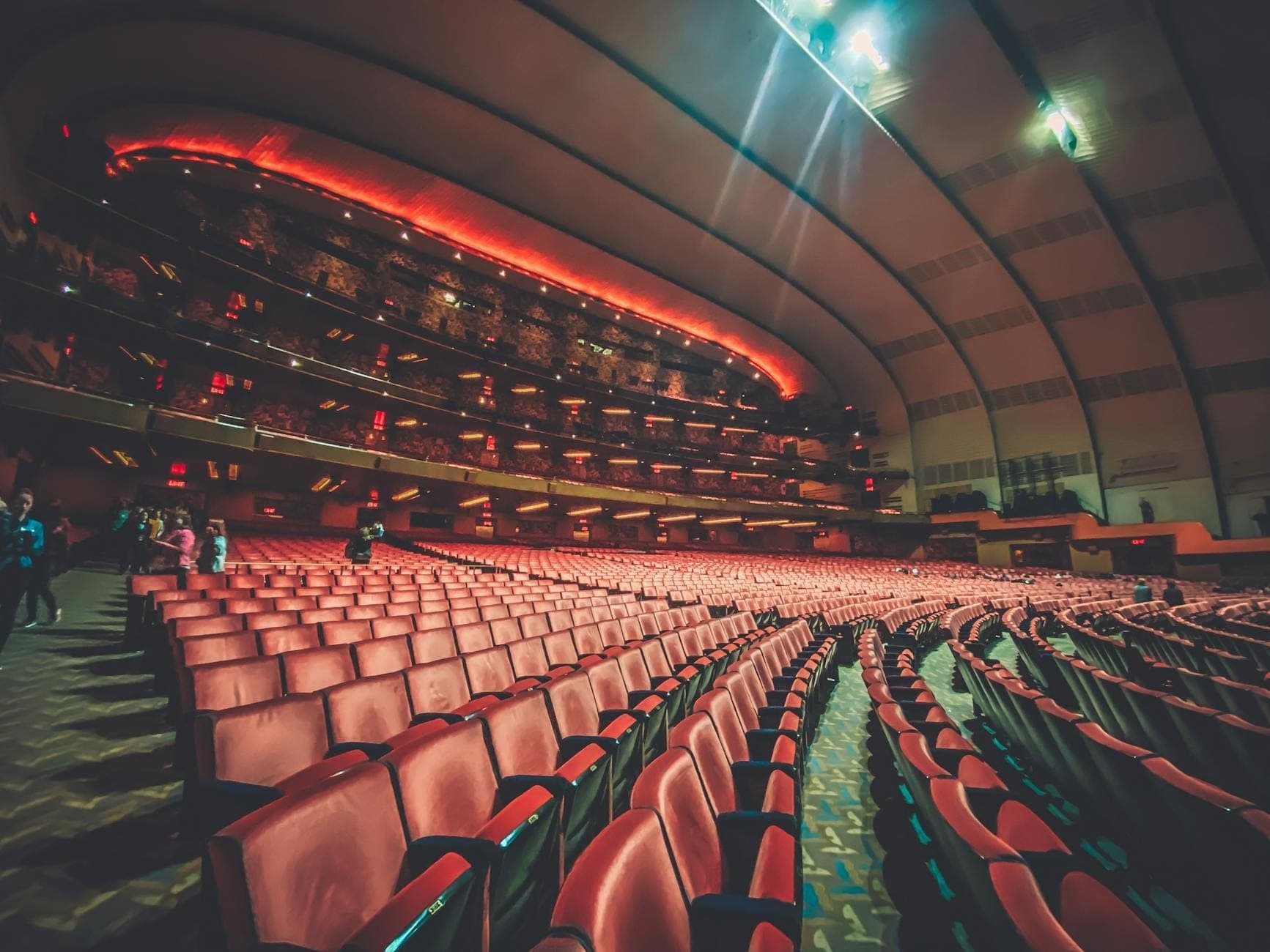 Vista grandangolare di un grande auditorium moderno con sedute rosse e balconi su più livelli, che mostra la disposizione dei posti e l'architettura della struttura.