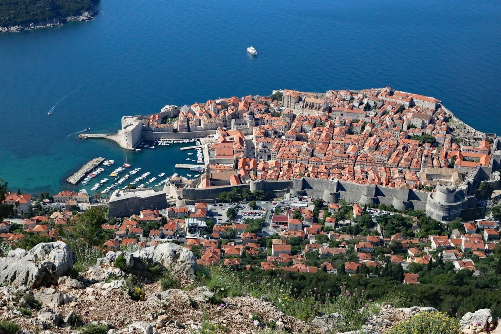 Vista aérea del puerto y la marina de Gruž: barcos atracados, el barrio residencial de alrededor, las murallas de la ciudad y el brillante mar Adriático en un día despejado.