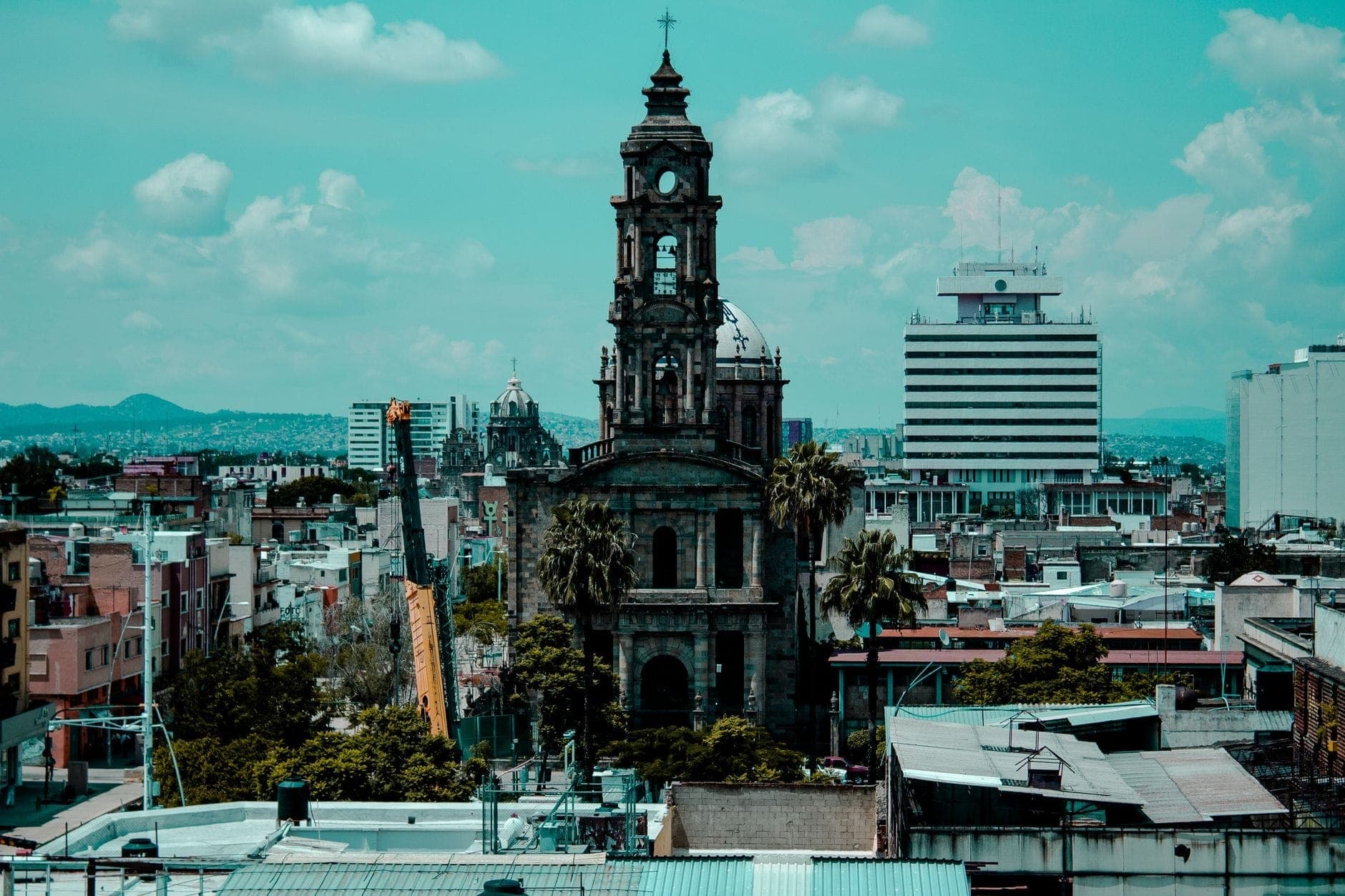 มุมมองทางอากาศของเส้นขอบฟ้าเมือง Guadalajara ที่มีหอคอยโบสถ์เก่าแก่ล้อมรอบด้วยอาคารในเมืองภายใต้ท้องฟ้าสีฟ้ามีเมฆ