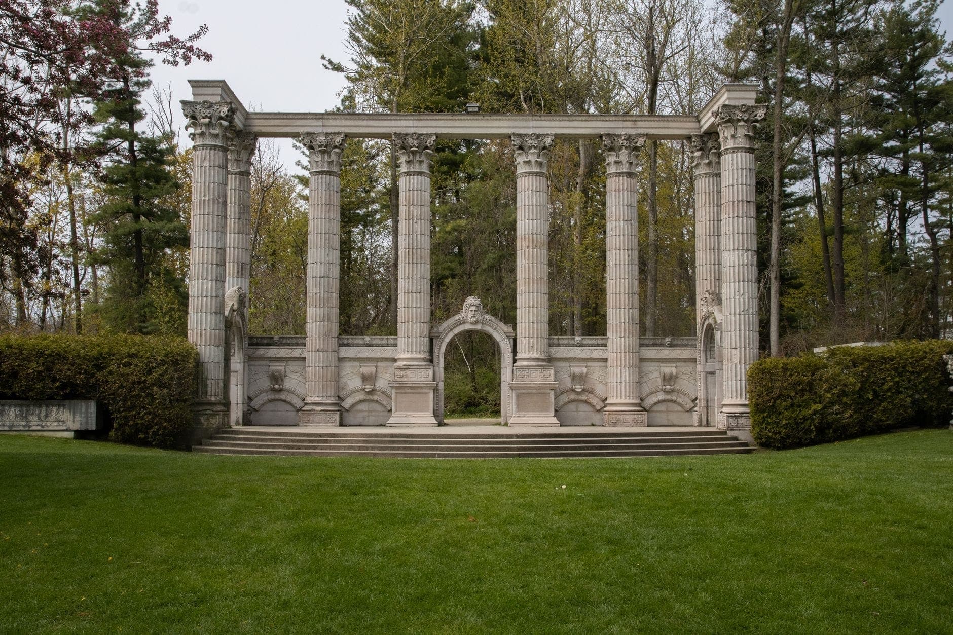 Colonne e archi in pietra provenienti da storici edifici di Toronto, disposti in una radura erbosa al Guild Park and Gardens, circondati da alberi e vegetazione.