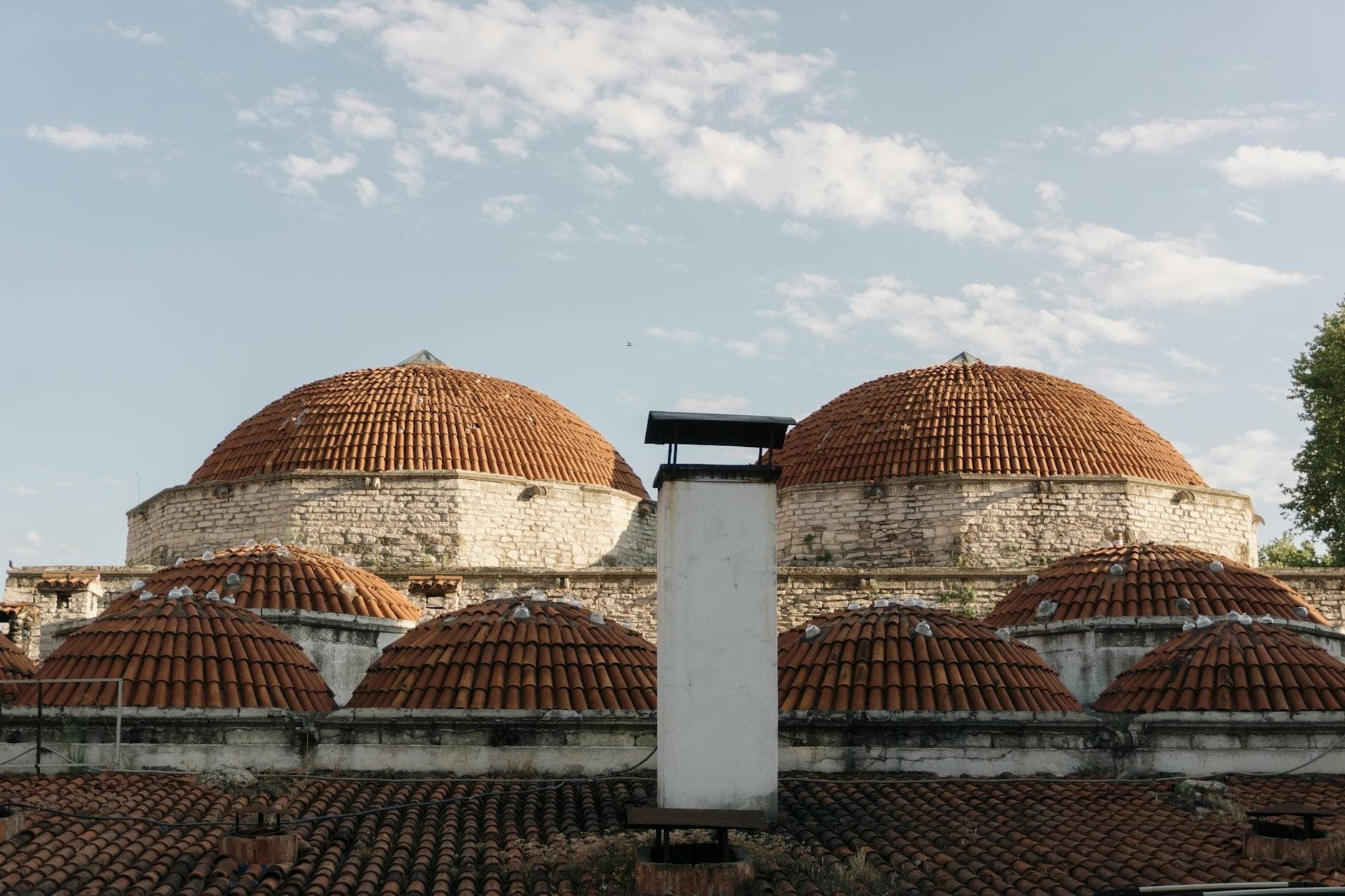 Vue extérieure d'un bain ottoman historique avec plusieurs toits en dôme et des briques patinées par le temps, sous un ciel bleu.