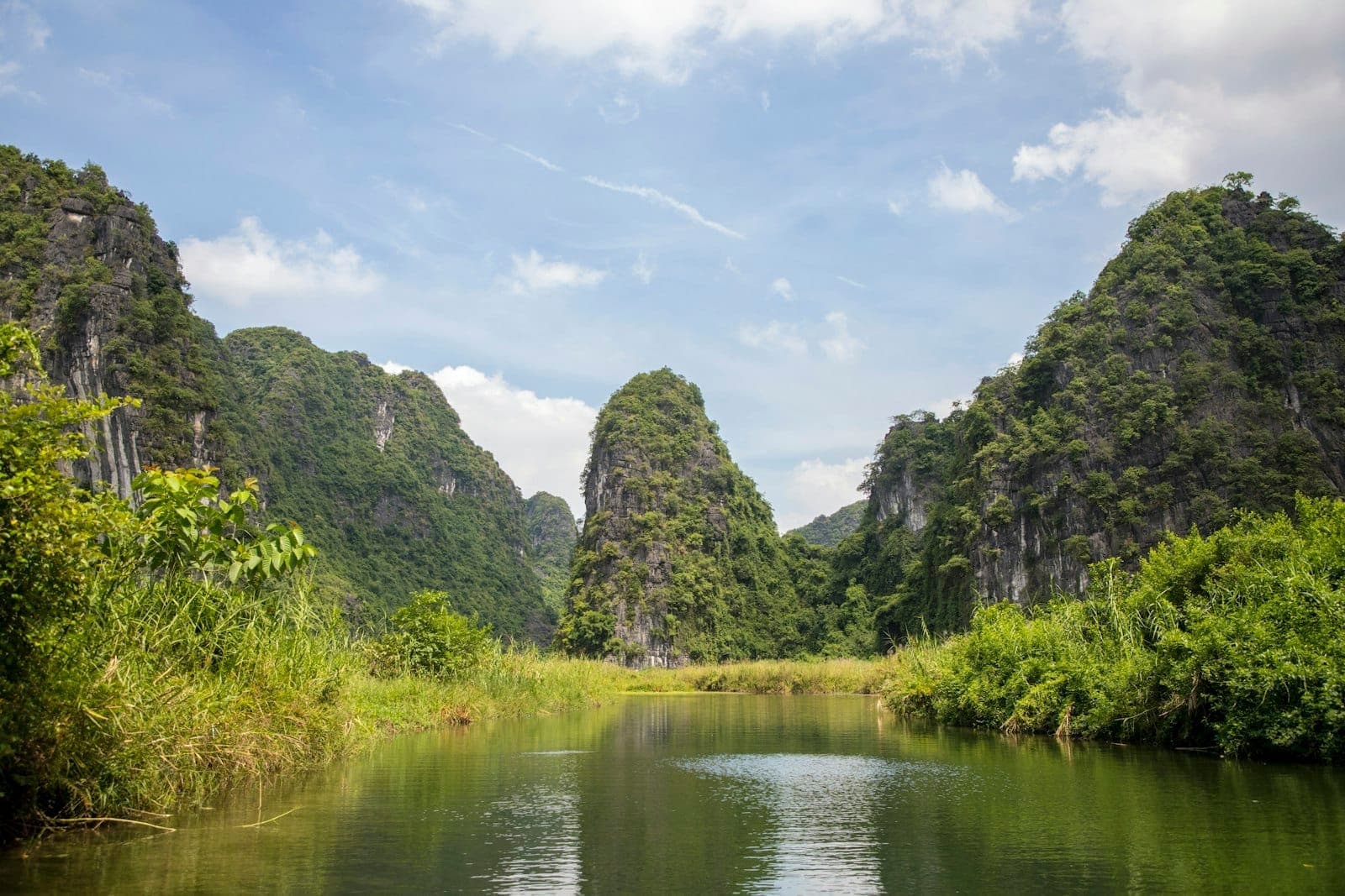 แม่น้ำคดเคี้ยวผ่านภูเขาหินปูนสีเขียวชอุ่มใต้ท้องฟ้าสีครามใน Ninh Binh จุดหมายทริปเดย์ทริปยอดนิยมจาก Hanoi