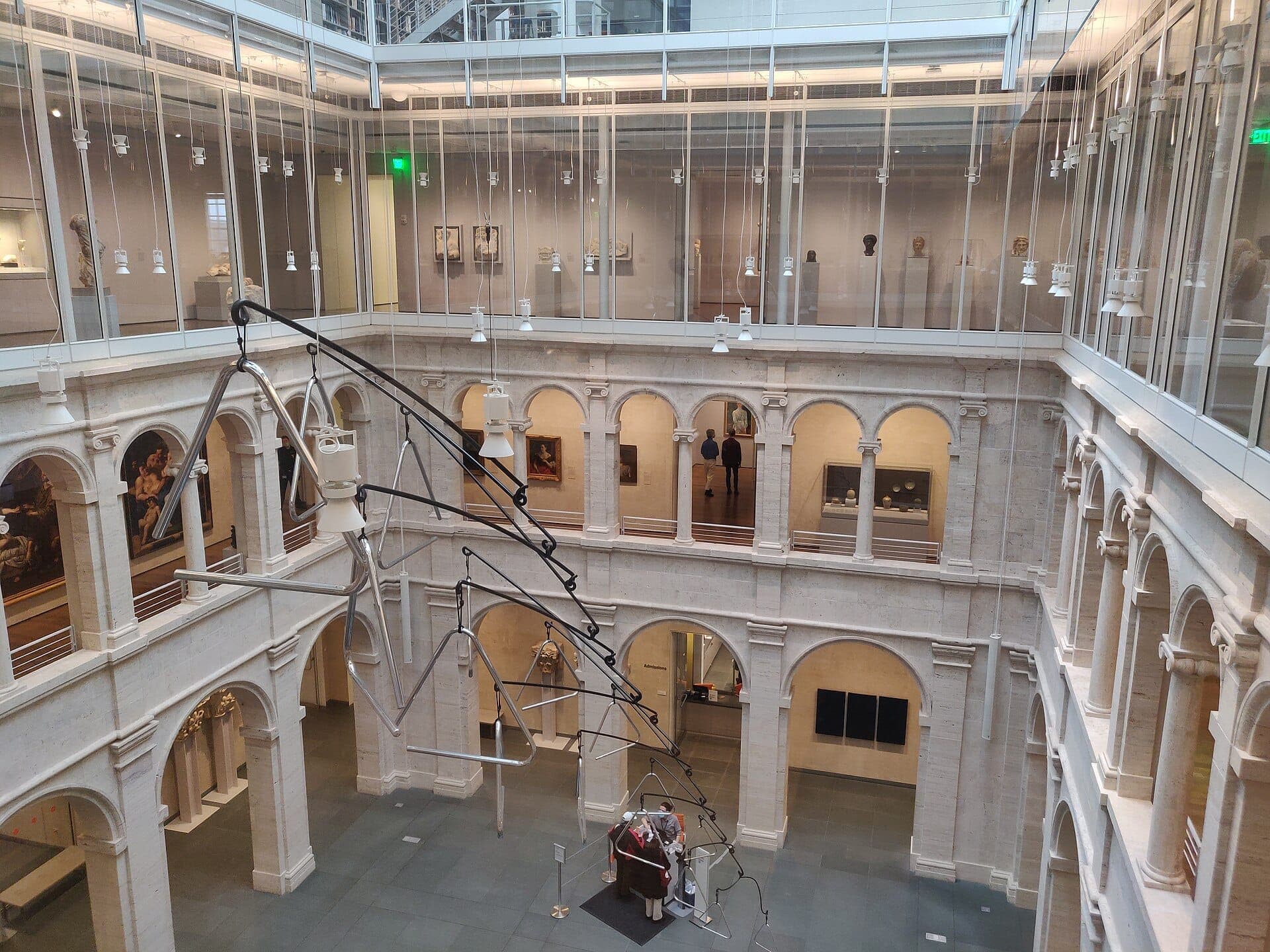 La cour centrale des Harvard Art Museums présente des galeries en pierre voûtées, des parois vitrées et une grande sculpture contemporaine suspendue sous des plafonds éclairés par des verrières.