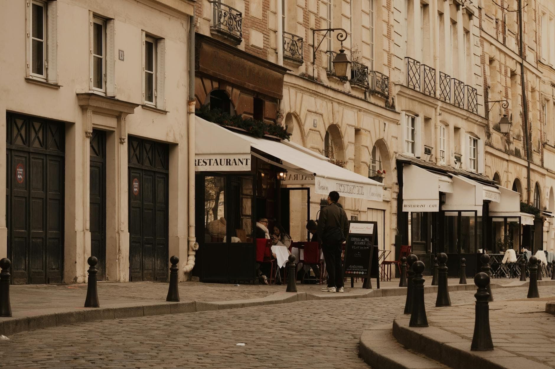 Enge Kopfsteinpflasterstraße in Paris mit historischen Gebäuden, einem gemütlichen Restaurant und einigen Fußgängern, die eine dorfartige Atmosphäre schaffen.
