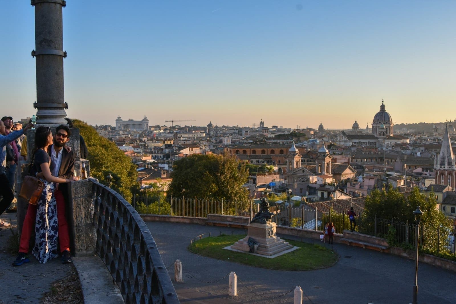 Orang-orang menikmati panorama kota Roma yang indah saat matahari terbenam dari teras di puncak bukit dengan kubah dan atap yang terlihat.