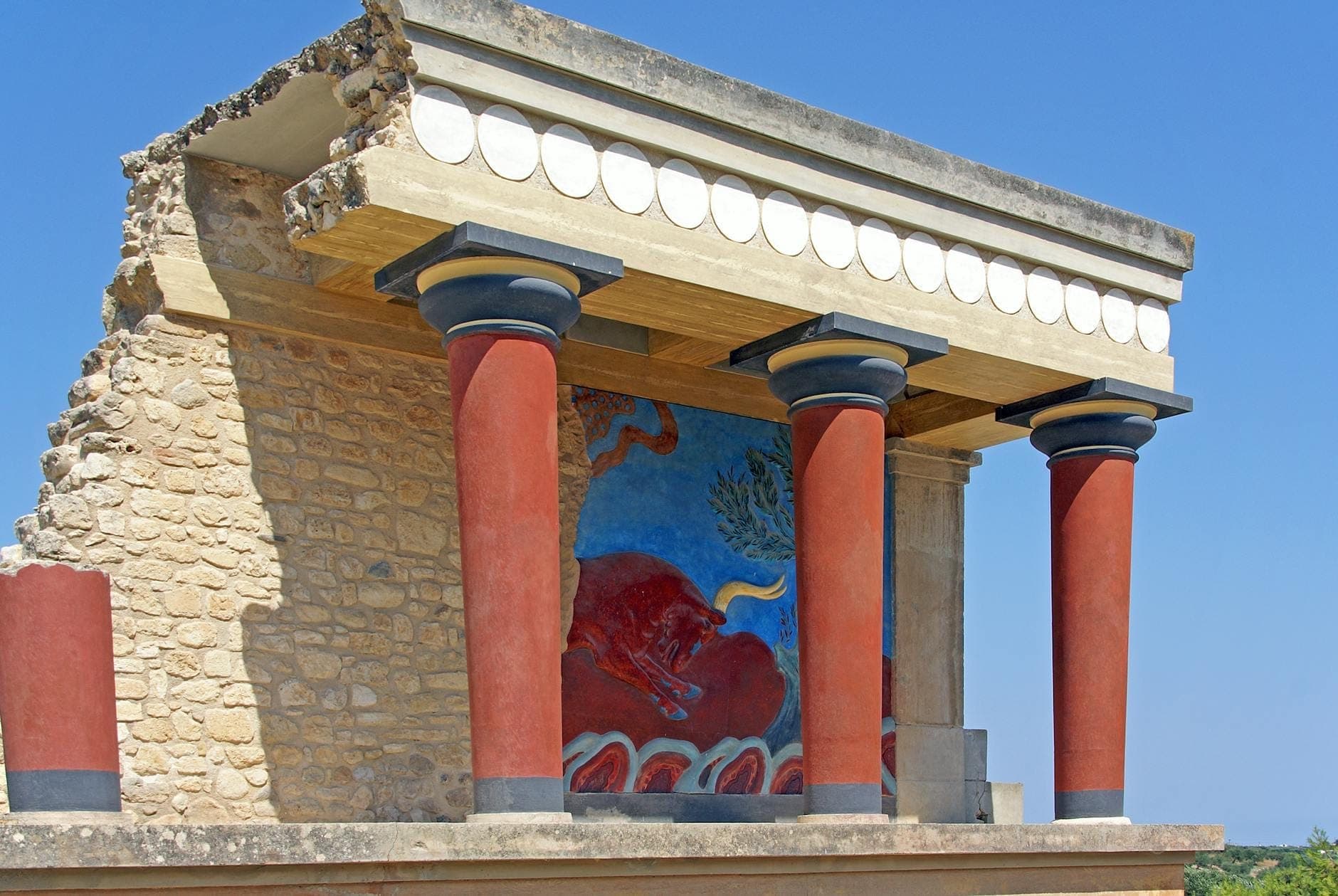 Ruinas bien conservadas del palacio minoico de Knossos en Creta, con distintivas columnas rojas y coloridos detalles de frescos en un día soleado.