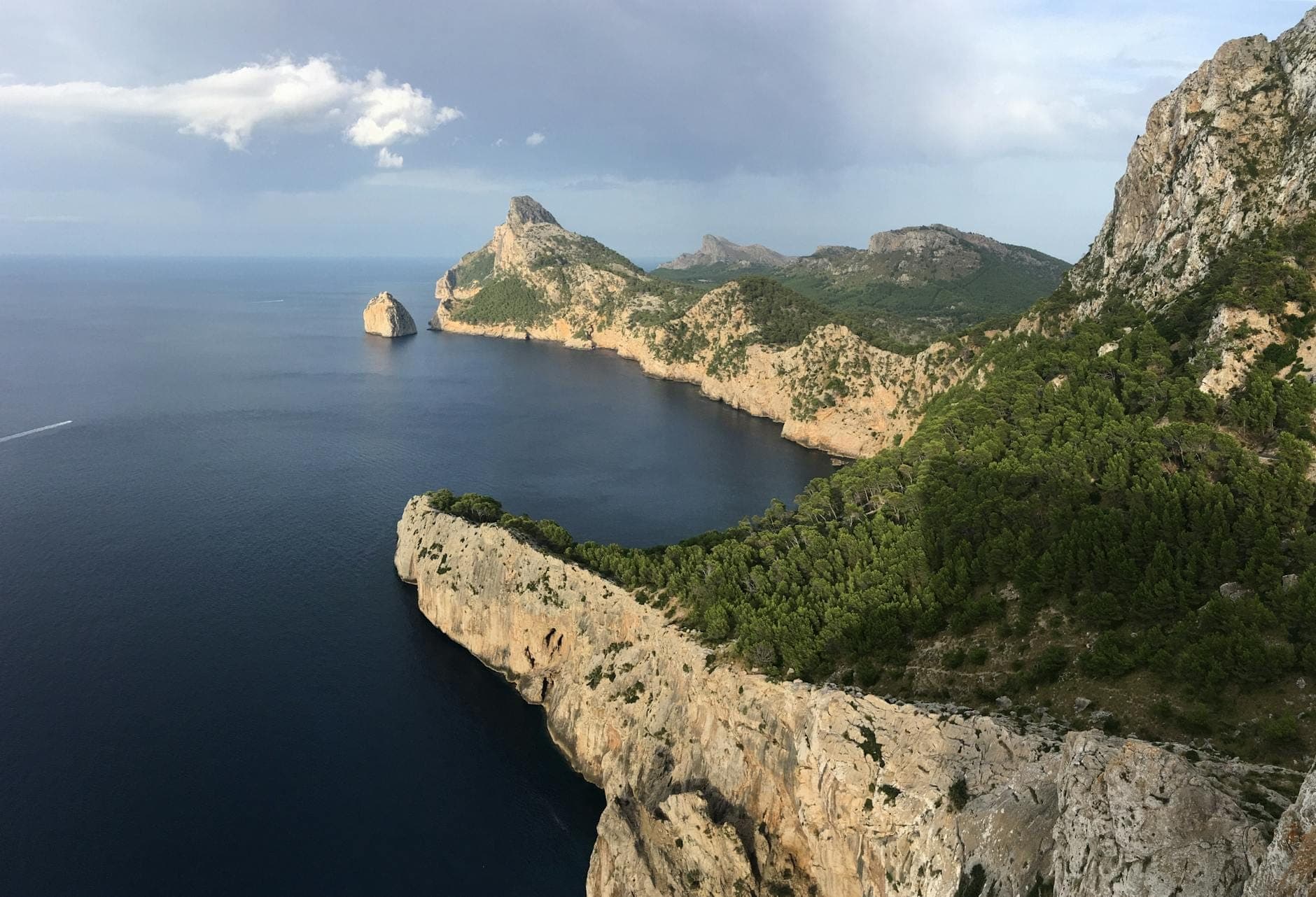 Costa spettacolare con ripide scogliere rocciose e colline verdi che incontrano il mare vicino alla penisola di Formentor nel nord di Maiorca sotto un cielo nuvoloso.
