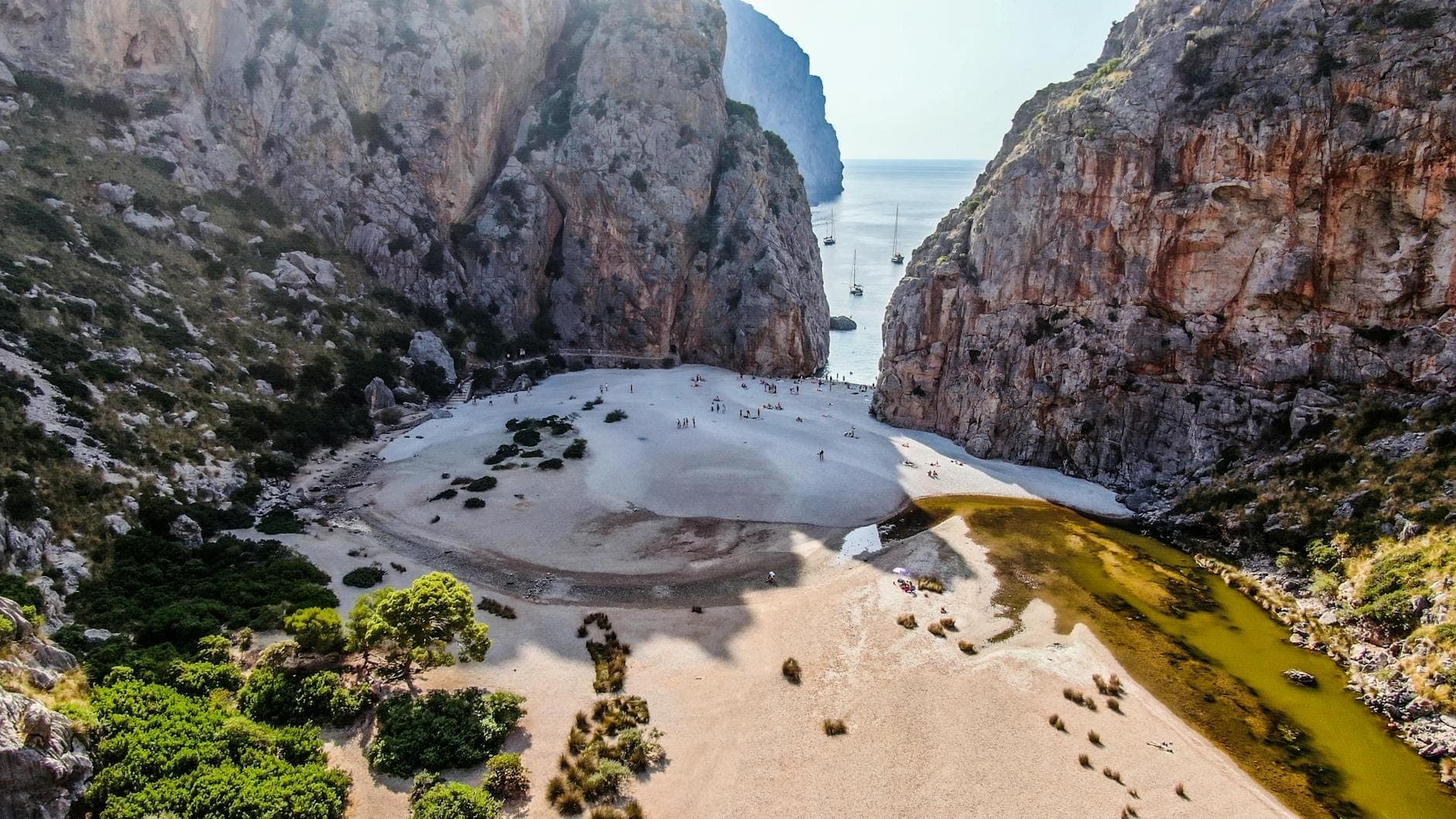 Drammatica gola calcarea che si apre sul mare con scogliere a picco, un'area sabbiosa e un ruscello, probabilmente l'iconico canyon di Sa Calobra a Maiorca.