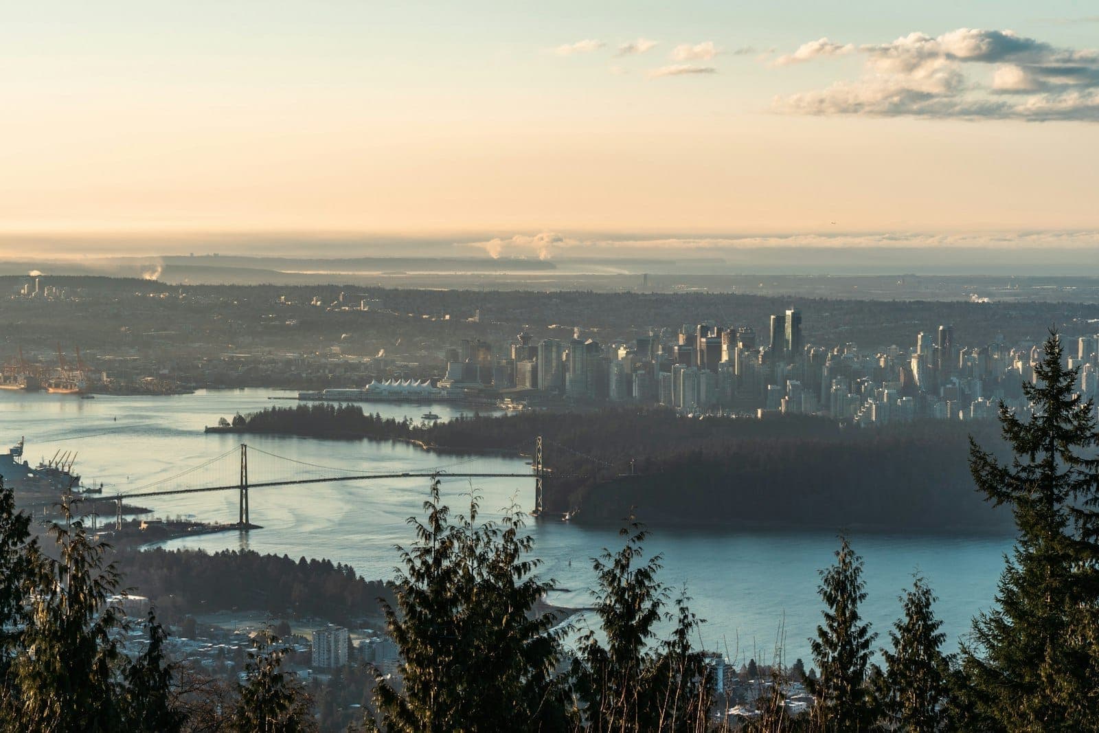 วิวพาโนรามาของตัวเมืองแวนคูเวอร์และสะพาน Lions Gate มองจากเส้นทางเดินป่าในป่าเขา ช่วงพระอาทิตย์ขึ้น เห็นแม่น้ำกับเส้นขอบฟ้าไกลสุดลูกหูลูกตา