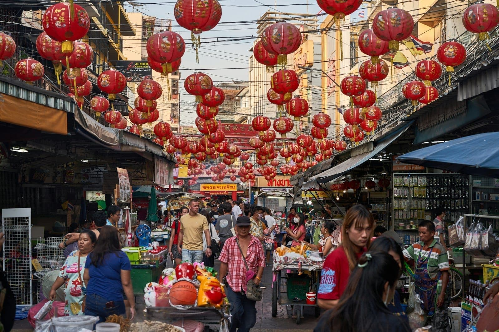 Movimentado mercado de rua em Cholon, Cidade de Ho Chi Minh, com lanternas vermelhas penduradas, compradores agitados e bancas de vendedores vibrantes durante o dia.