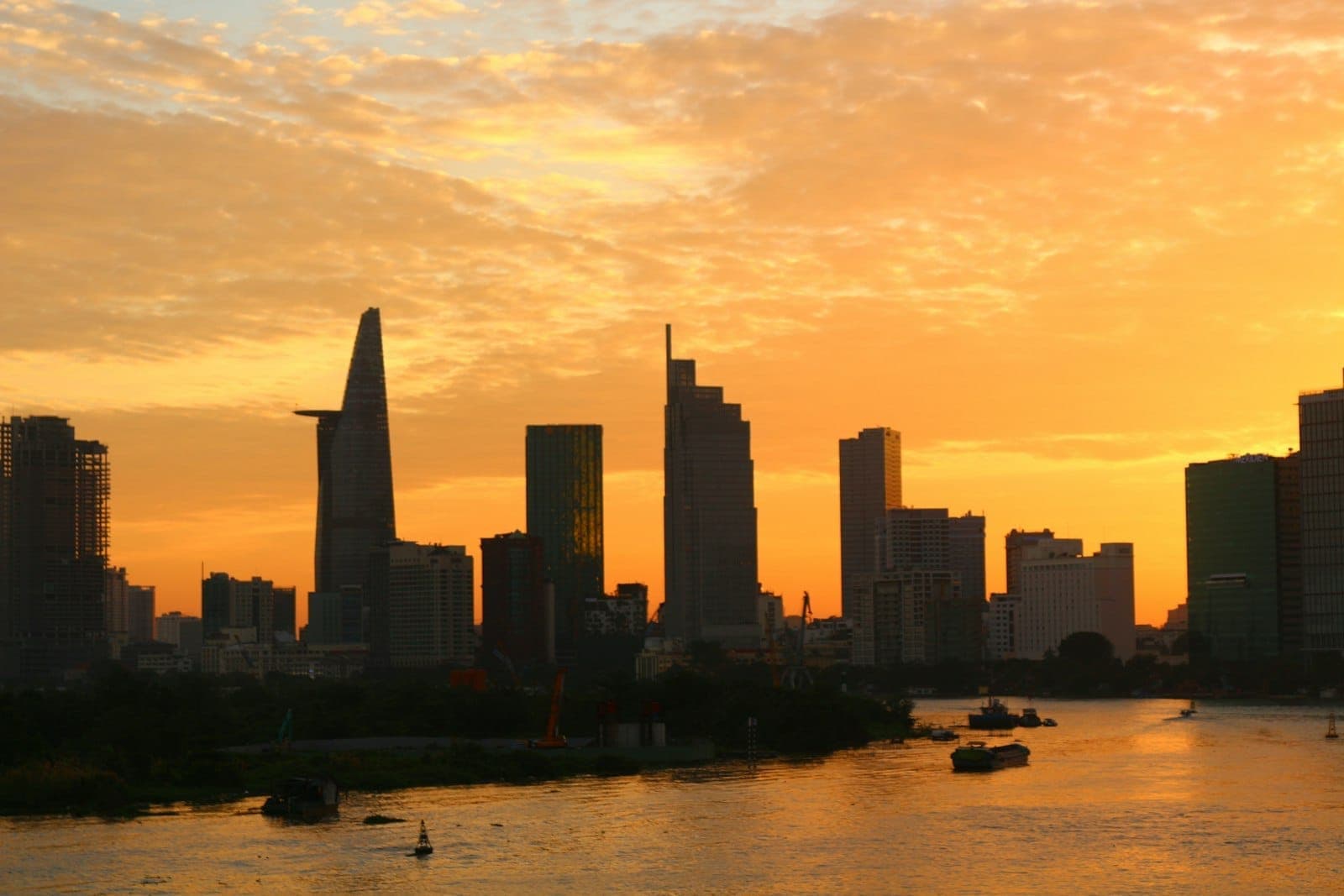 Skyline de Ho Chi Minh City ao pôr do sol com edifícios modernos e o rio Saigon em primeiro plano