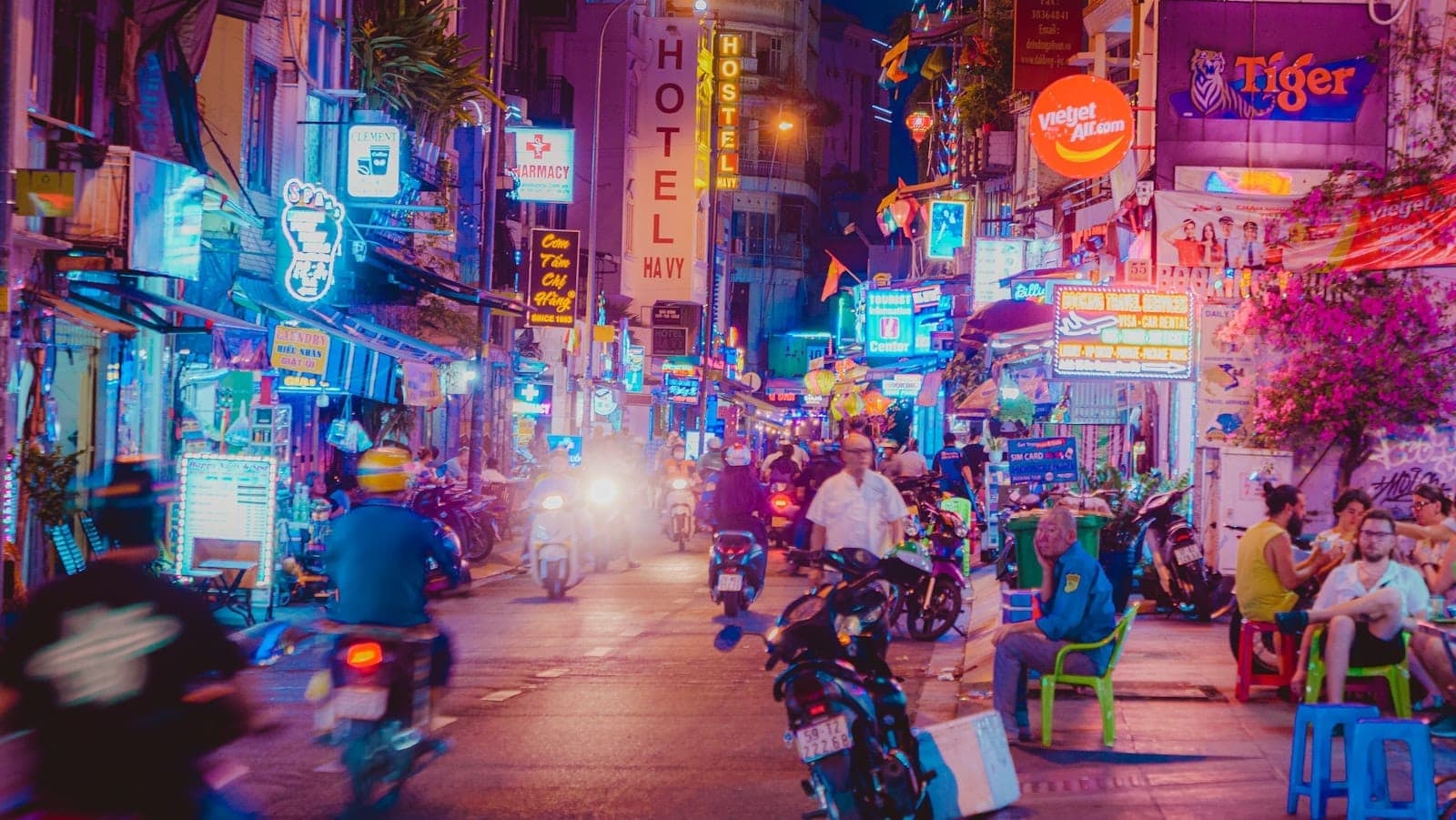 Ho Chi Minh City'de neon ışıklı barlar, motosikletler ve 1. Bölge'de sokakta sosyalleşen insanlarla dolu hareketli gece hayatı sahnesi.