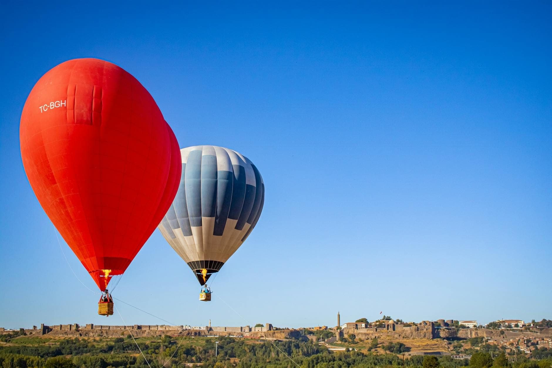 Zwei bunte Heißluftballons schweben über einer malerischen Landschaft mit historischen Gebäuden und strahlend blauem Himmel auf Mallorca – perfekt als Reiseinspiration.