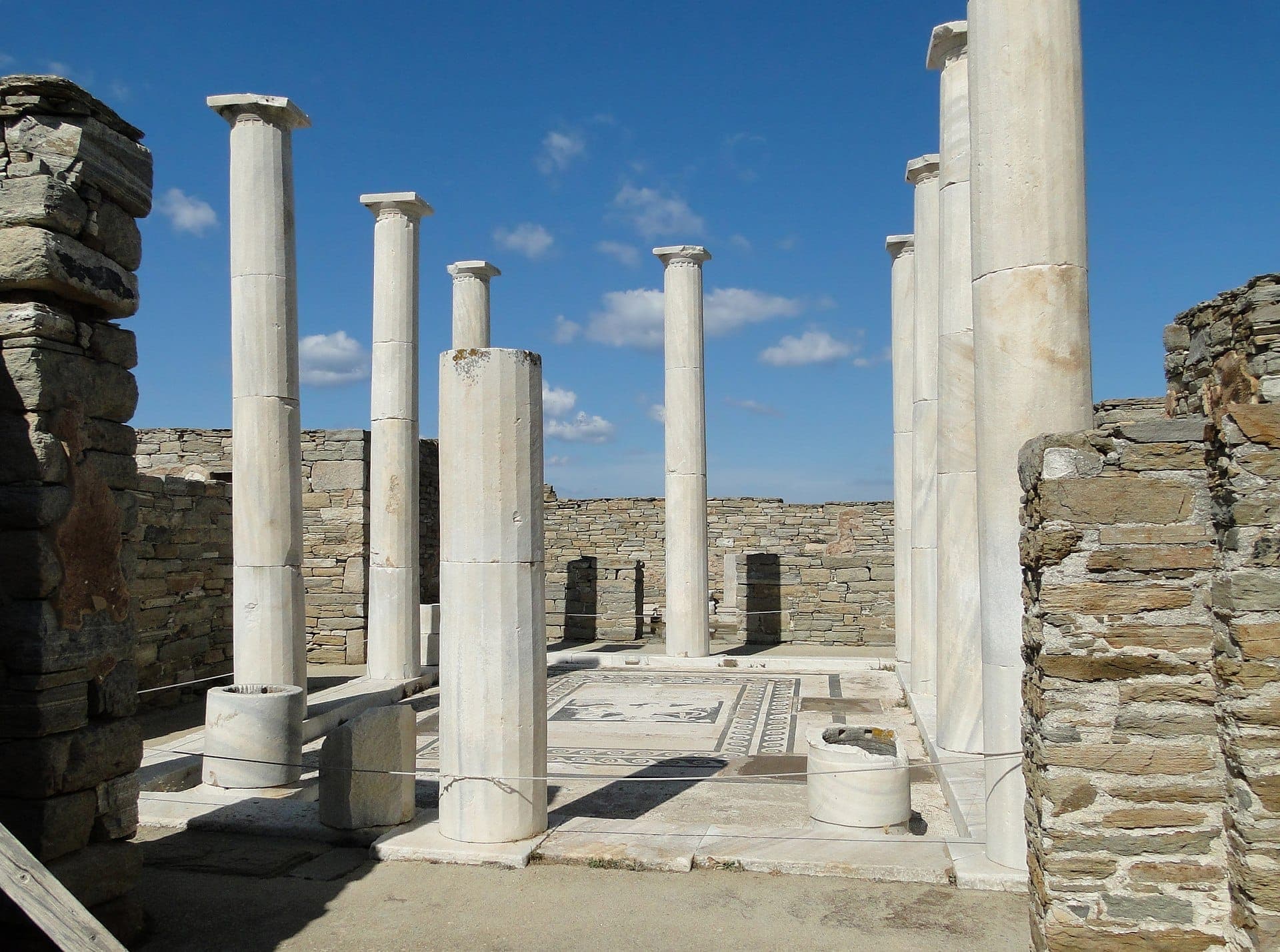 Marmorsäulen und alte Steinmauern umgeben den berühmten Mosaikhof im Haus des Dionysos auf Delos unter einem klaren blauen Himmel.