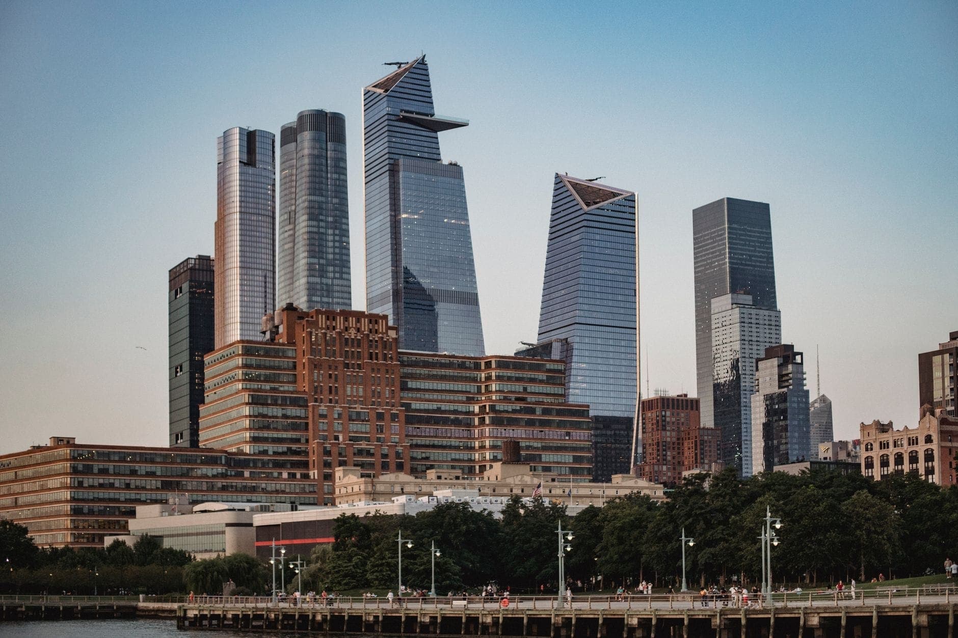 ภาพกว้างของตึกระฟ้าทันสมัยใน Hudson Yards คู่กับอาคารอิฐและเรือนยอดไม้ริมแม่น้ำฮัดสัน ฝั่งตะวันตกแมนฮัตตัน