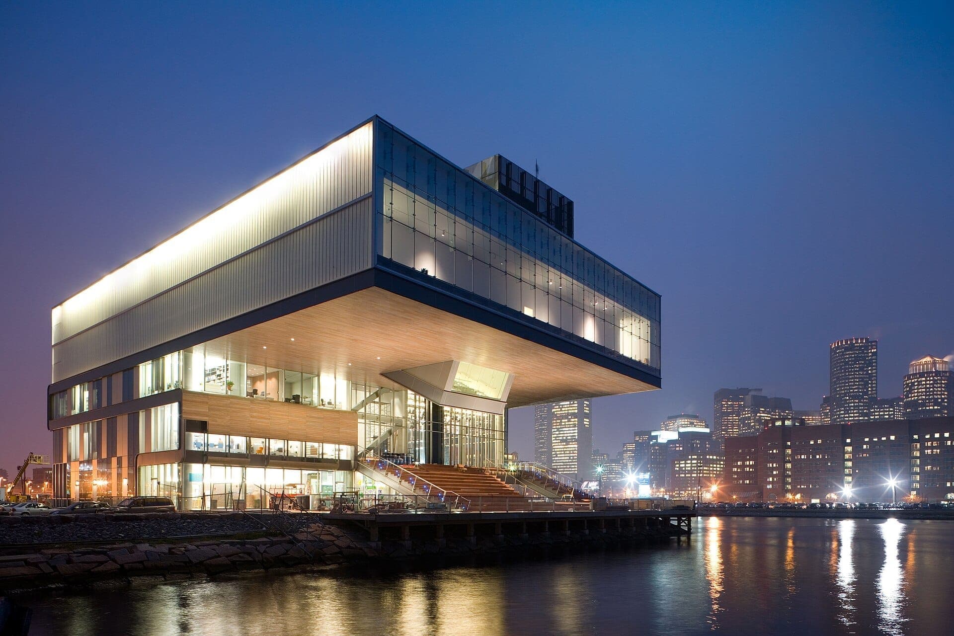 L'Institute of Contemporary Art Boston au crépuscule, son bâtiment moderne en verre en porte-à-faux au-dessus du front de mer, avec les lumières de la ville se reflétant sur l'eau.
