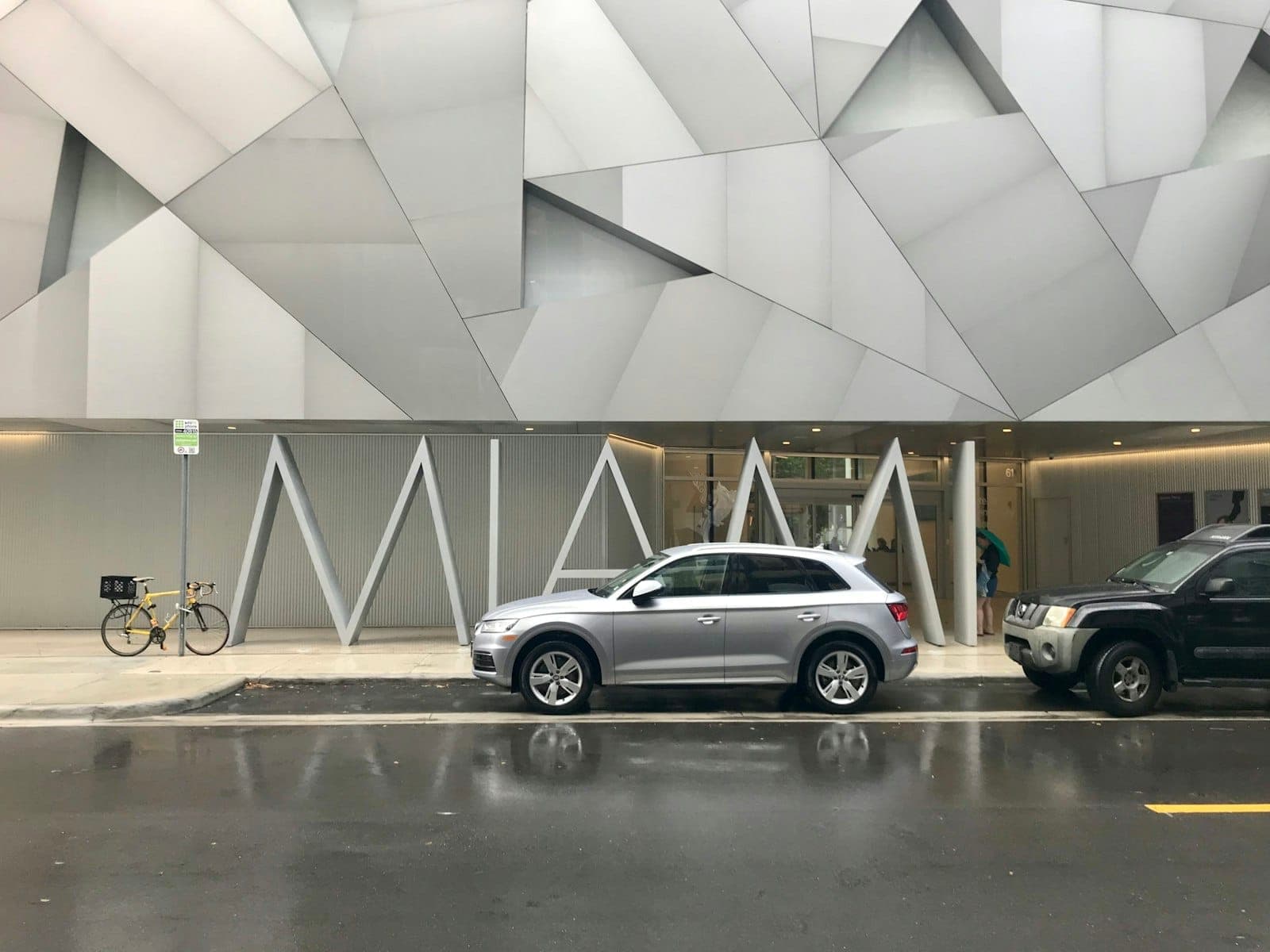 Façade extérieure de l'Institute of Contemporary Art Miami avec son architecture géométrique moderne, des voitures garées et un vélo sous la pluie.