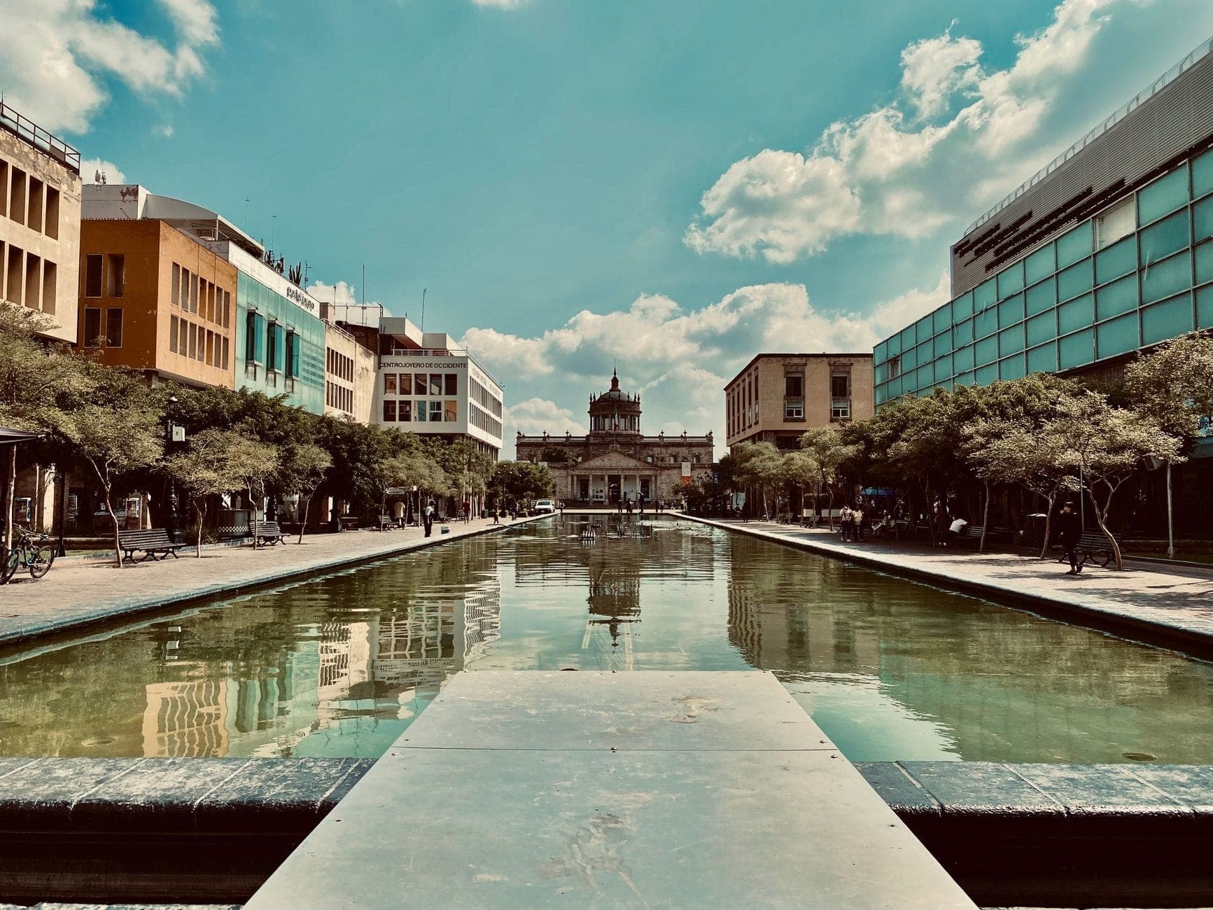 วิวกลางวันใจกลาง Guadalajara ถนนคนเดินกว้าง อาคารสีสันสดใส สระน้ำ และสถานที่ประวัติศาสตร์ Hospicio Cabañas อยู่ไกล ๆ ใต้ท้องฟ้าสีฟ้า
