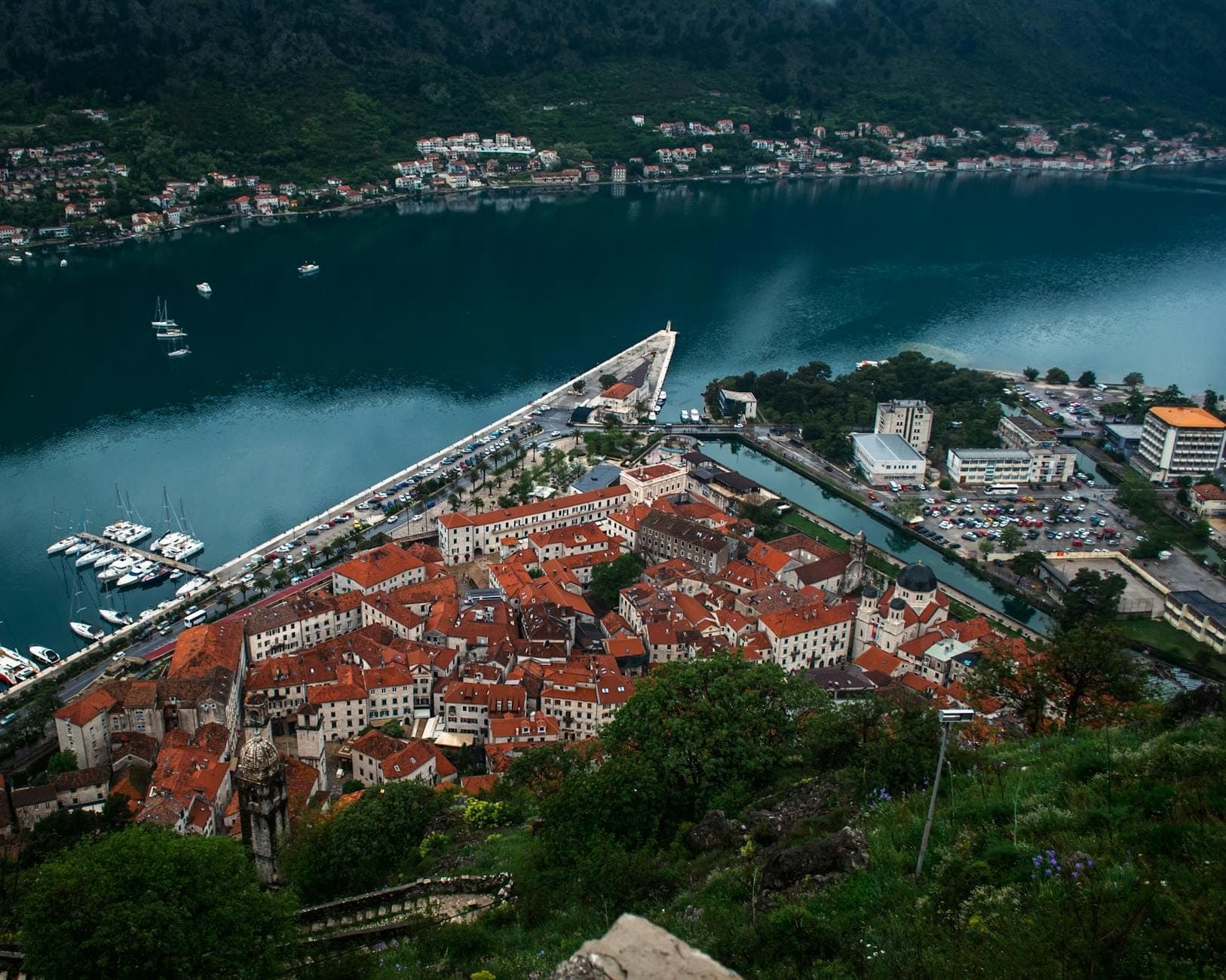 Vue en hauteur de la vieille ville de Kotor avec ses toits rouges et la baie, entourée de montagnes, montrant les remparts et le front de mer.