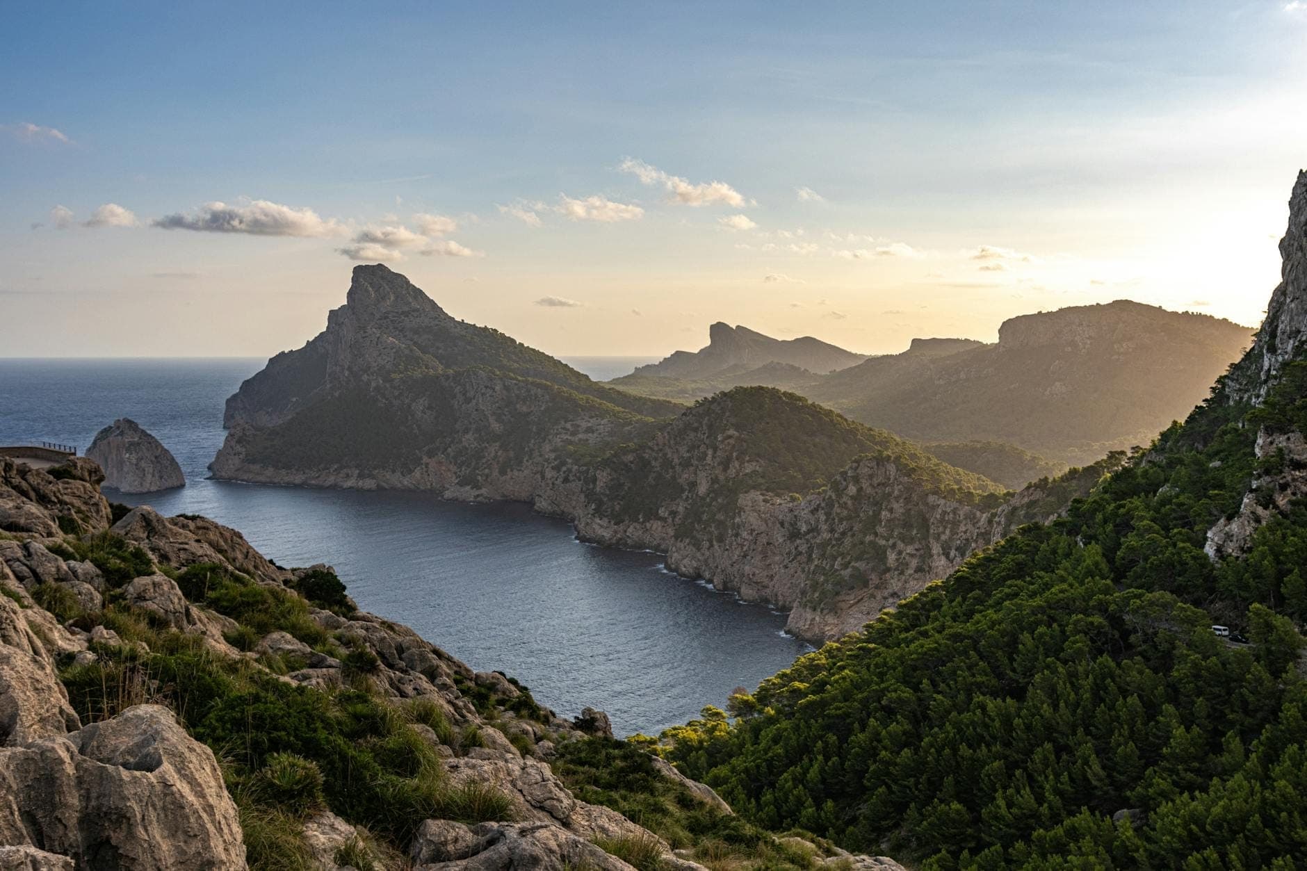 Klare Küstenansicht von Mallorca mit schroffen Klippen, üppigen grünen Hügeln und ruhigem Meer unter einem hellen Himmel, die saisonale Landschaftsvielfalt zeigend.