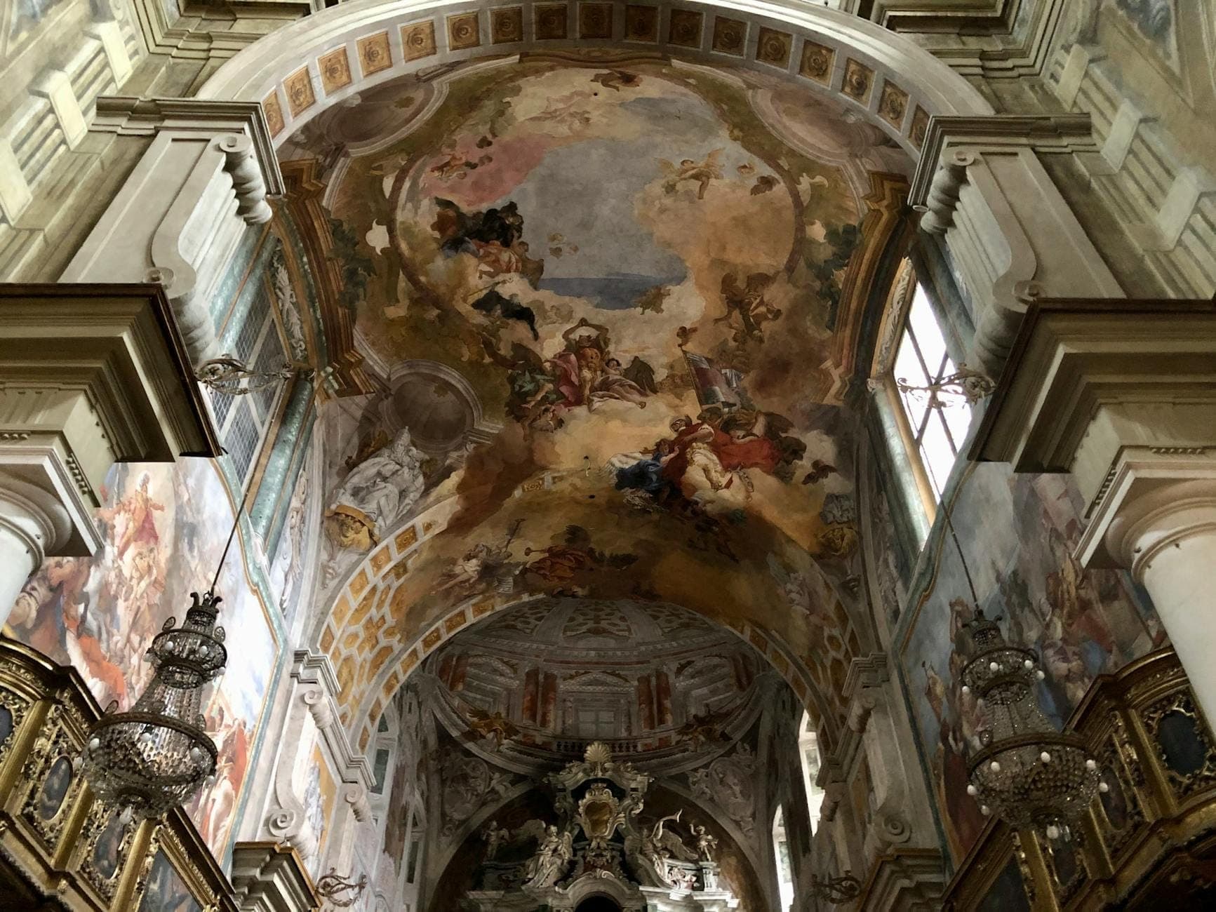 Vista interior de uma igreja histórica ricamente decorada em Nápoles, com afrescos ornamentados, lustres e arcos detalhados.