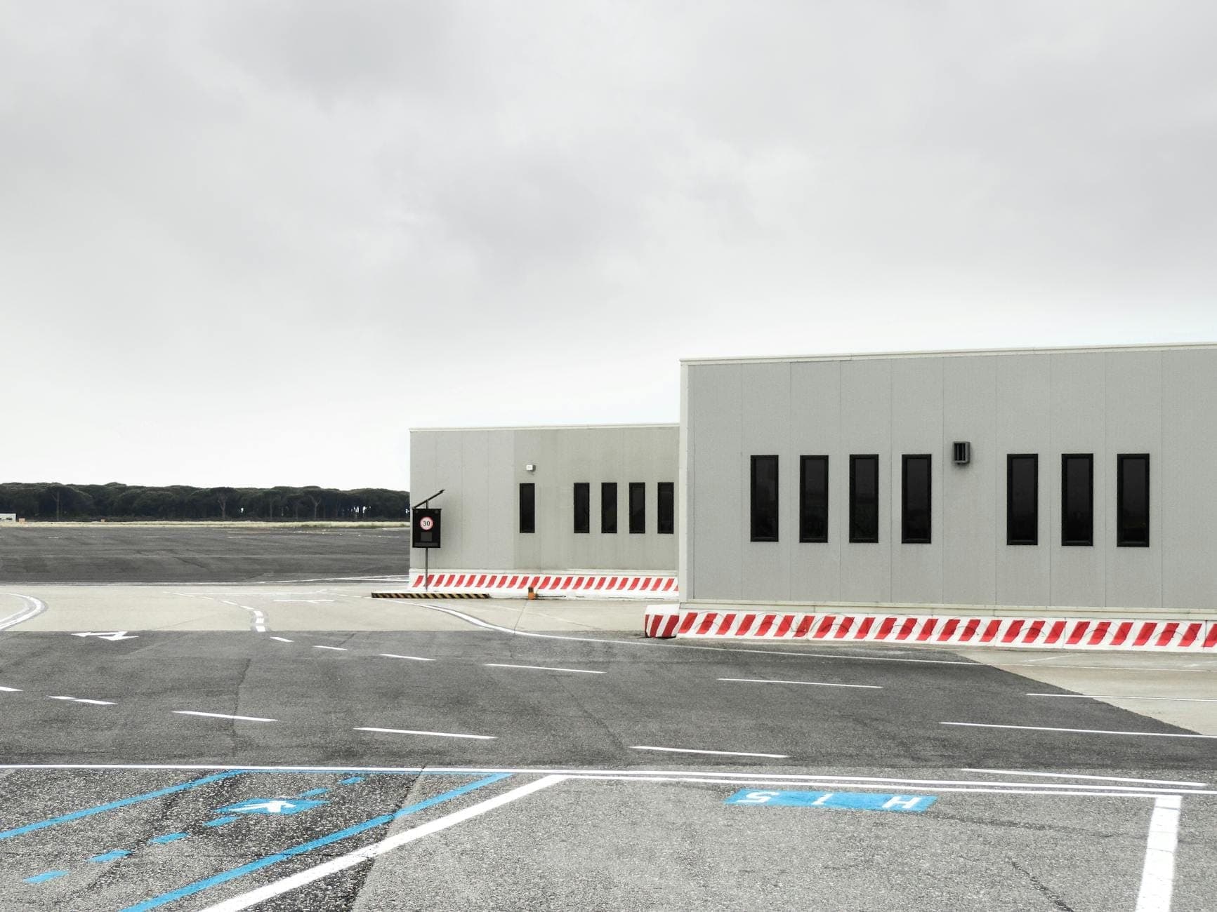 Vista de un pequeño edificio terminal de aeropuerto junto a una pista de aterrizaje vacía bajo un cielo nublado, que representa las instalaciones de transporte terrestre.