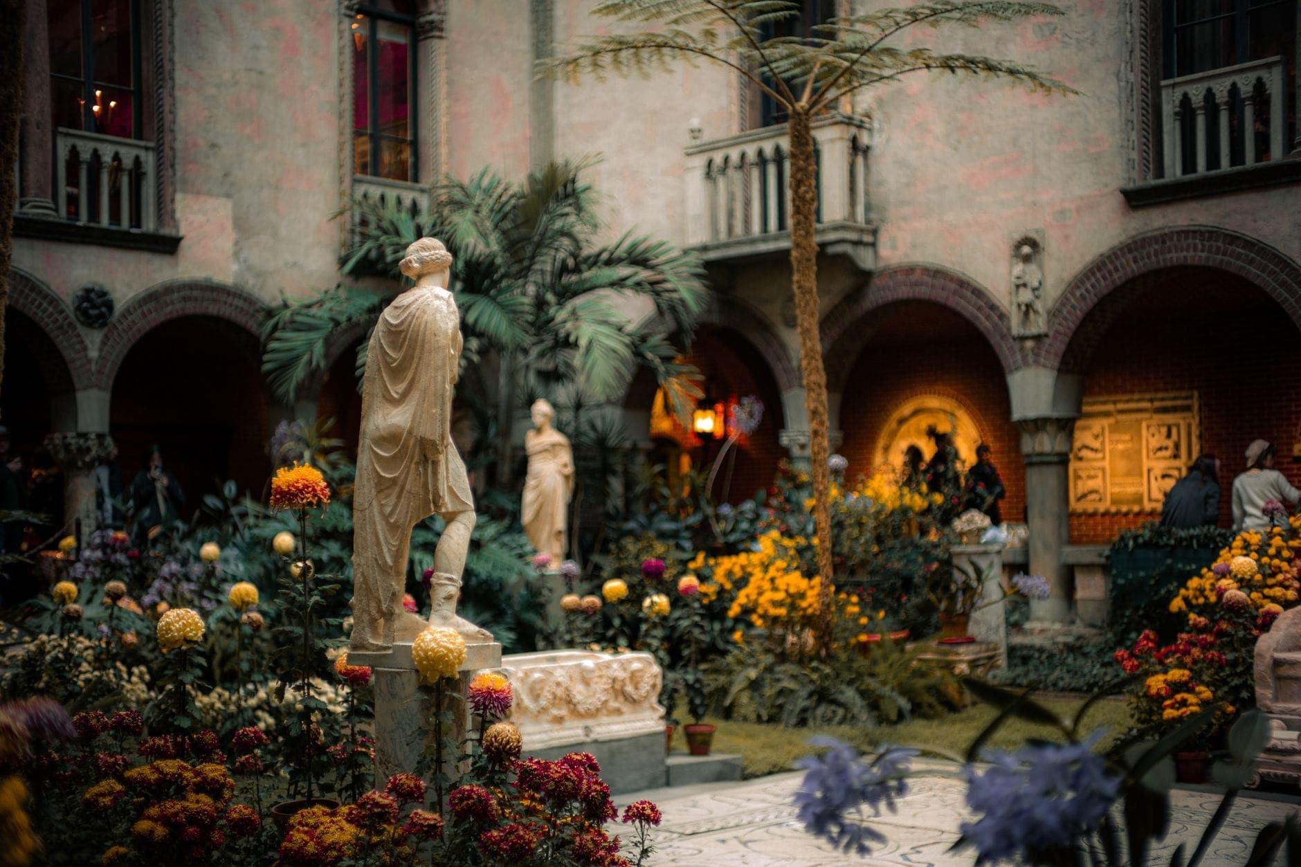 Cour intérieure luxuriante ornée de statues, de fenêtres arquées de style vénitien et d'une végétation abondante au musée Isabella Stewart Gardner.