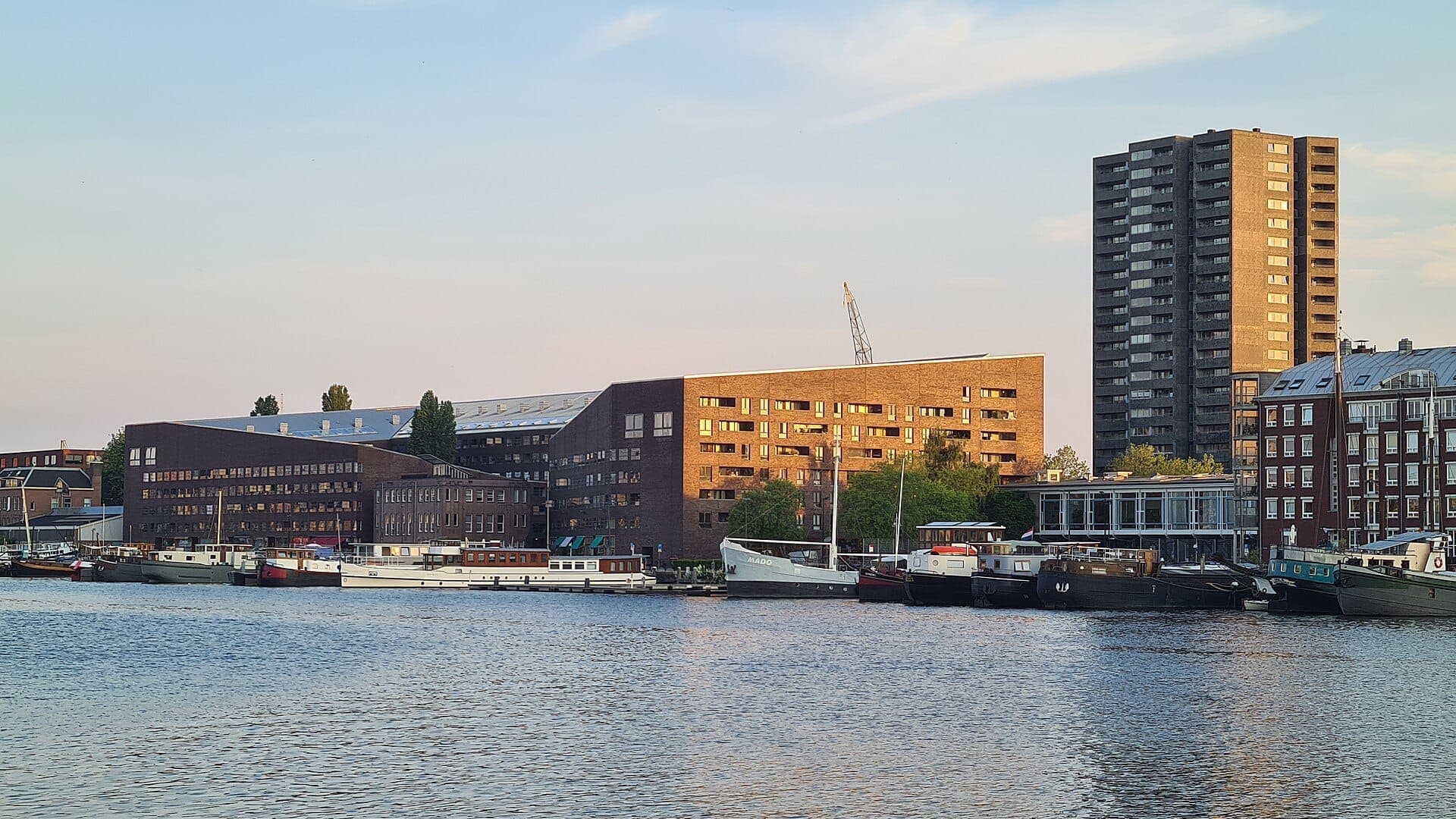 Moderne Wohngebäude und vertäute Boote säumen das Ufer von Java Island und KNSM Island in Amsterdam bei Sonnenuntergang.