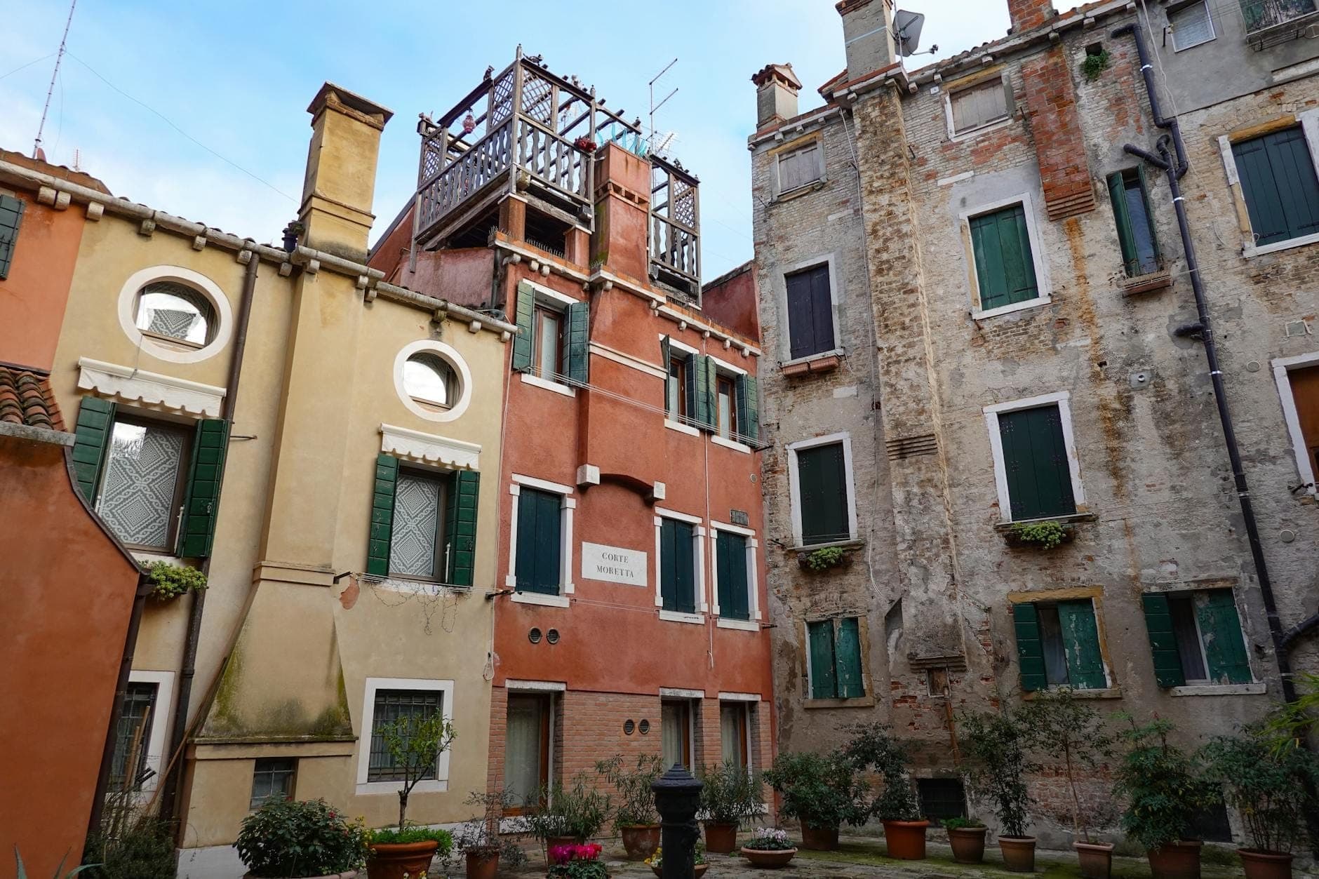 Makulay na mga puno ng gusali at mga napatigasin na bato na may berdeng mga shutter sa Jewish Ghetto ng Roma, nakapaligid sa isang maliit na looban na may mga halaman sa paso.