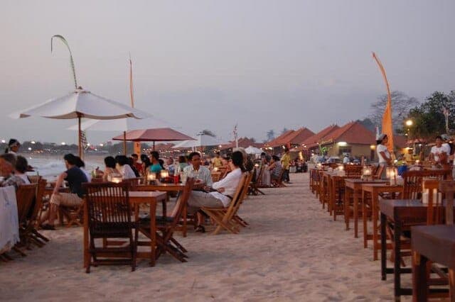 Grilled seafood dinner tables set on the sand at Jimbaran Bay in Bali with sunset light over the ocean