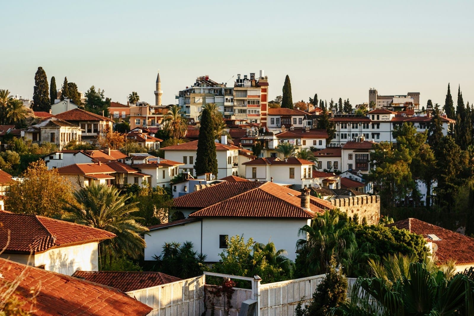 Blick über die rotgeziegelten osmanischen Dächer, Minarette und üppigen Bäume von Kaleiçi im goldenen Sonnenlicht – das historische Altstadtflair Antalyas.