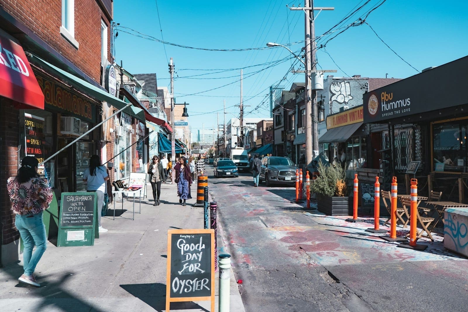 Una vivace scena di strada a Kensington Market con negozi colorati, insegne di caffè, pedoni e vetrine uniche in una giornata di sole a Toronto.