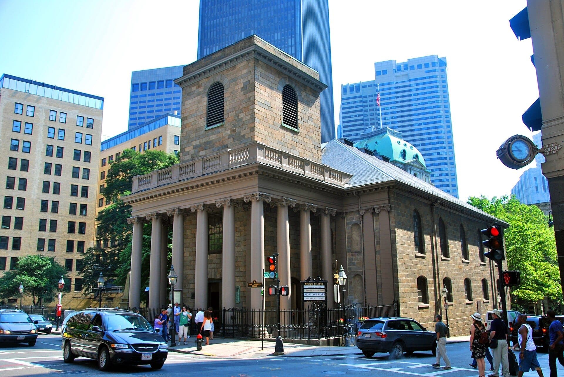 La King's Chapel à Boston, une église historique en granit avec de hautes colonnes, se dresse à une intersection animée entourée d'immeubles modernes du centre-ville.