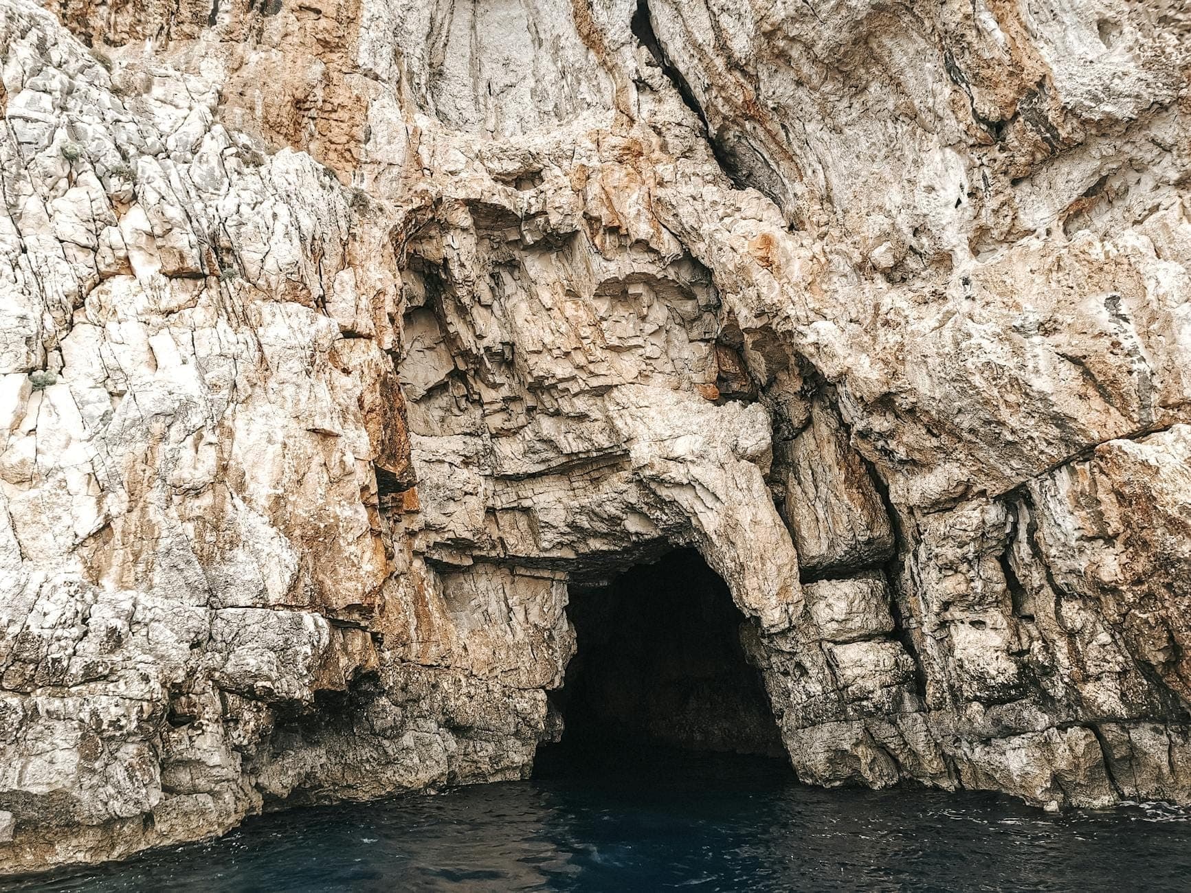 Entrée d'une grotte marine dans des falaises calcaires escarpées au-dessus d'eaux bleu profond par une journée ensoleillée.