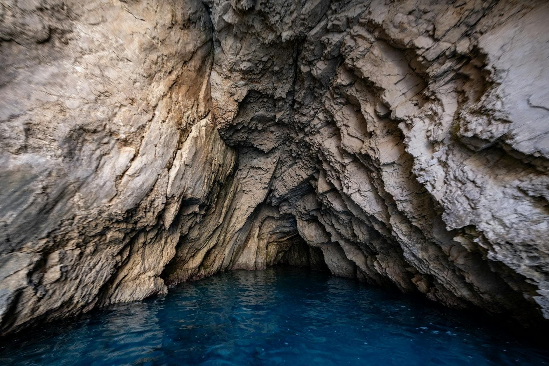 Intérieur d'une grotte côtière avec des parois rocheuses beiges accidentées et une eau bleu profond, montrant la vaste chambre que les visiteurs découvrent à l'intérieur.