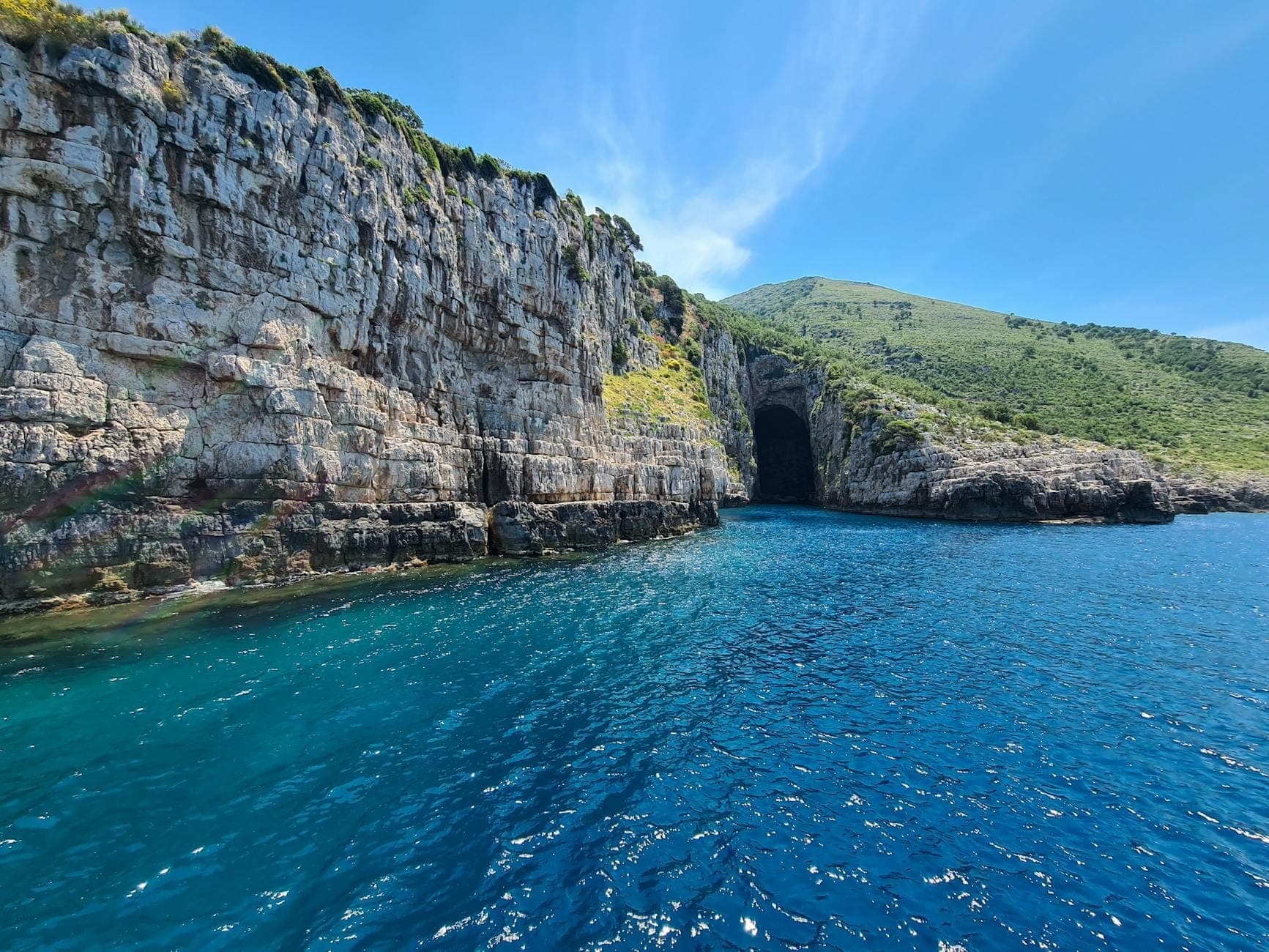 Falaises rocheuses et entrée de la Grotte Bleue près de Kotor, Monténégro, entourées d'eaux bleues cristallines et d'une végétation luxuriante sous un ciel lumineux.