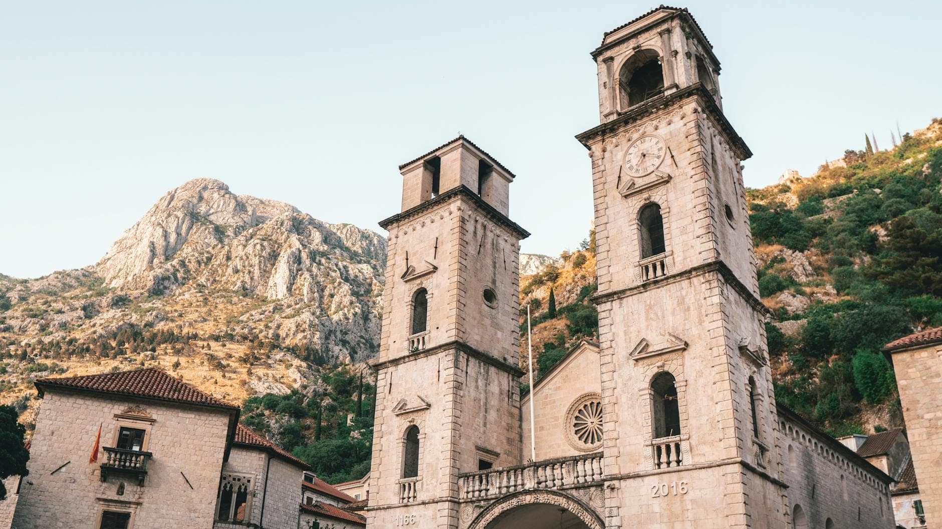 Vue de face d'une cathédrale romane avec deux hauts clochers dans la vieille ville historique de Kotor, sur fond de montagne.
