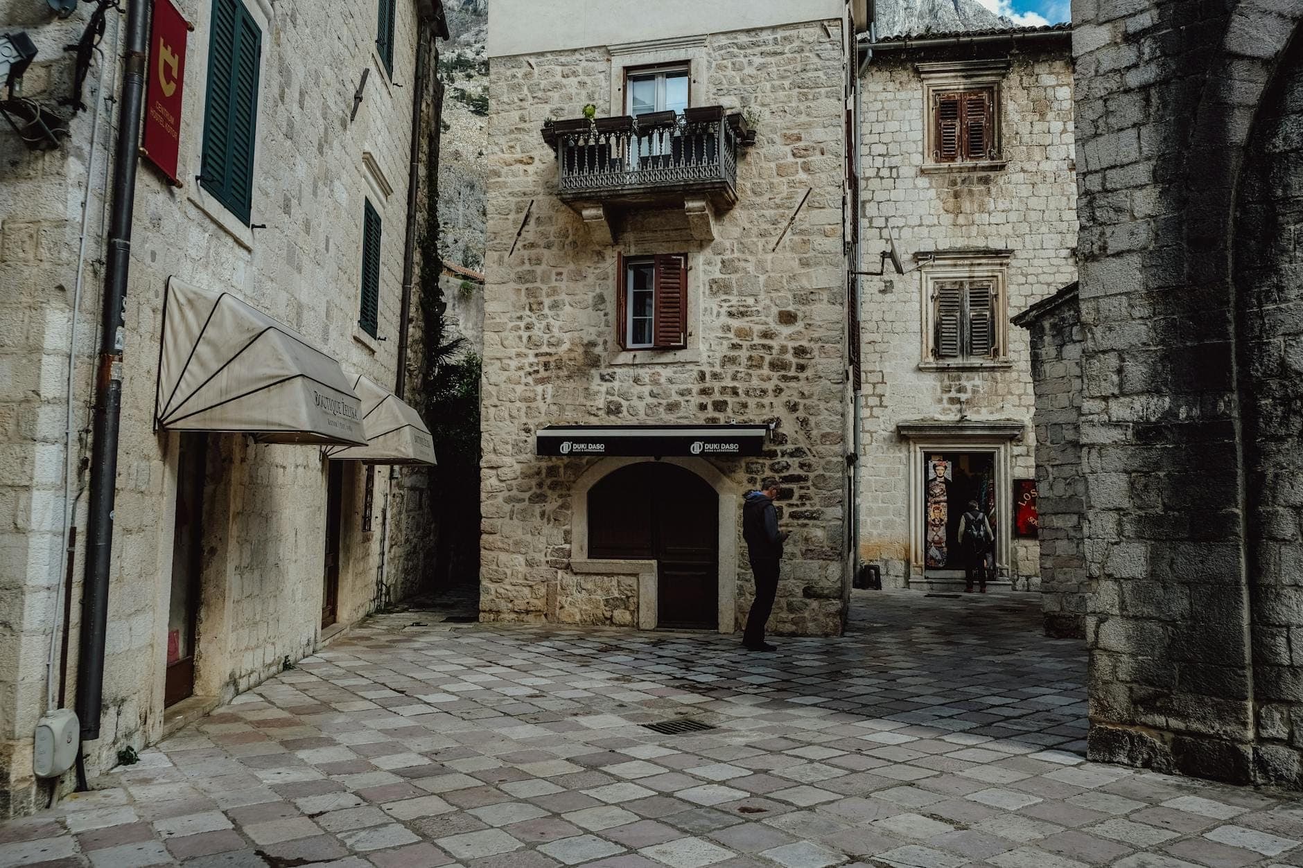 Cour en pierre tranquille dans la vieille ville de Kotor avec des ruelles étroites, des bâtiments historiques en pierre et quelques personnes, révélant son caractère résidentiel caché.