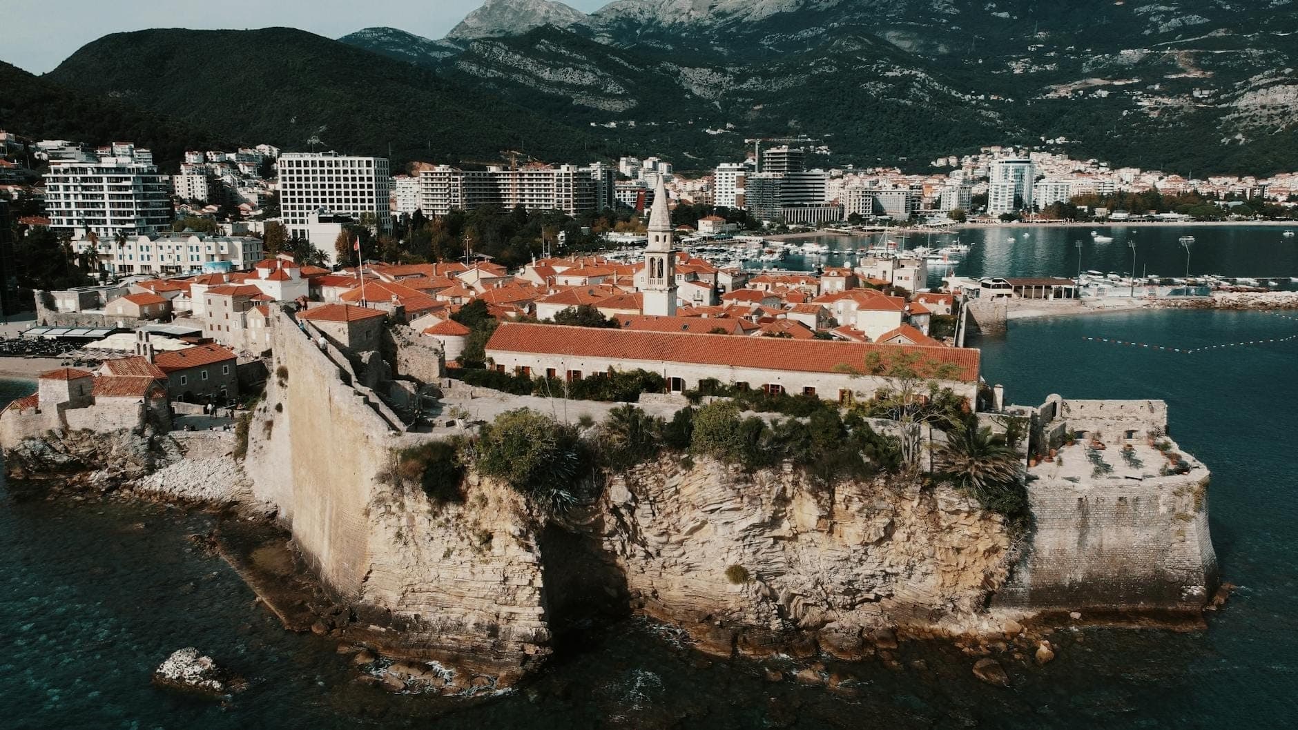 Vue aérienne de la vieille ville de Budva et de ses fortifications côtières avec les montagnes de la Baie de Kotor en arrière-plan, illustrant les points de vue voisins près de Kotor.