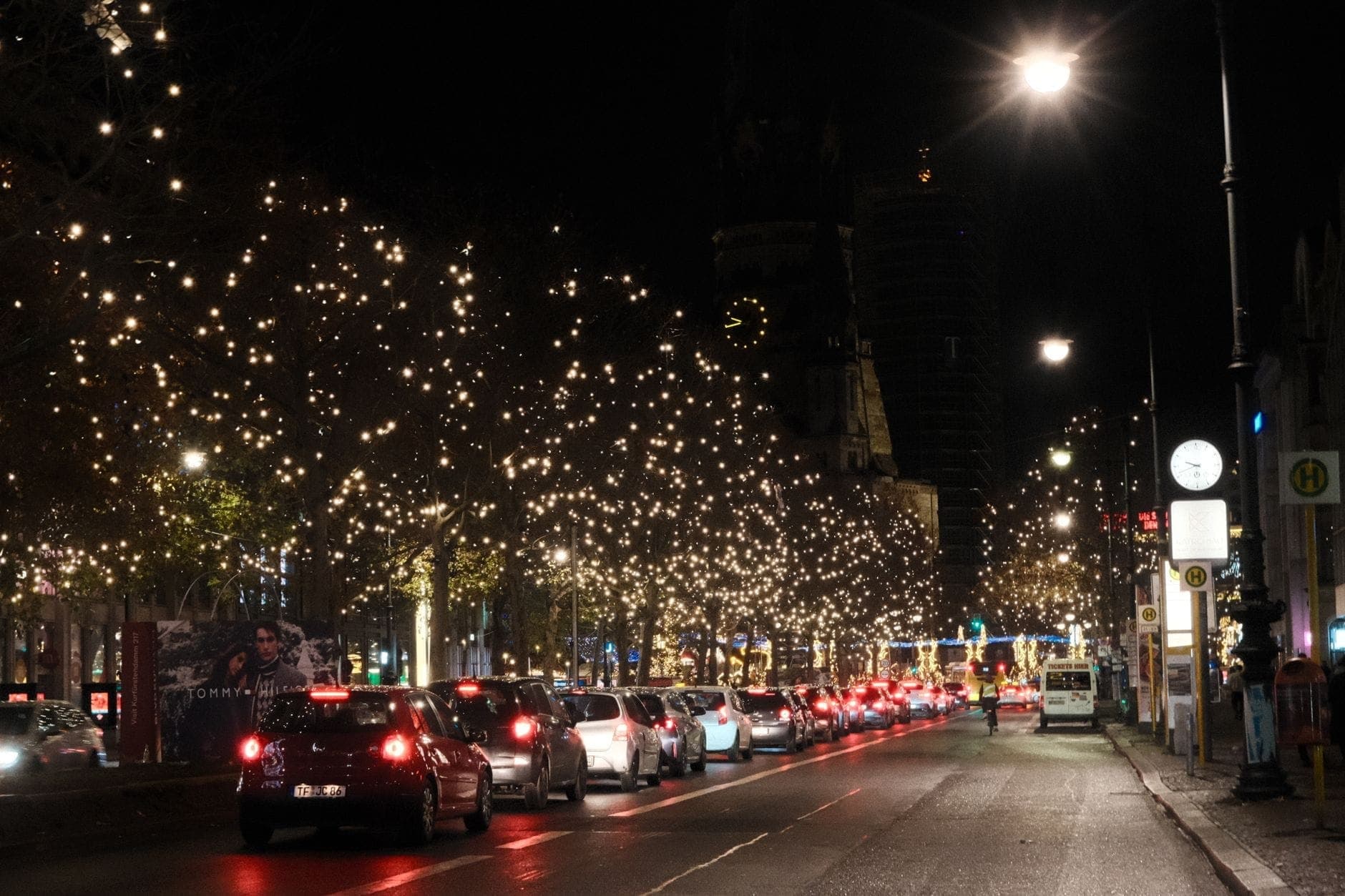 วิวกลางคืนของ Kurfürstendamm ไฟประดับต้นไม้สว่าง รถยนต์ขนาบสองข้างถนนใหญ่ ถ่ายทอดบรรยากาศสนุกมีชีวิตชีวาและสีสันเทศกาลของเบอร์ลิน