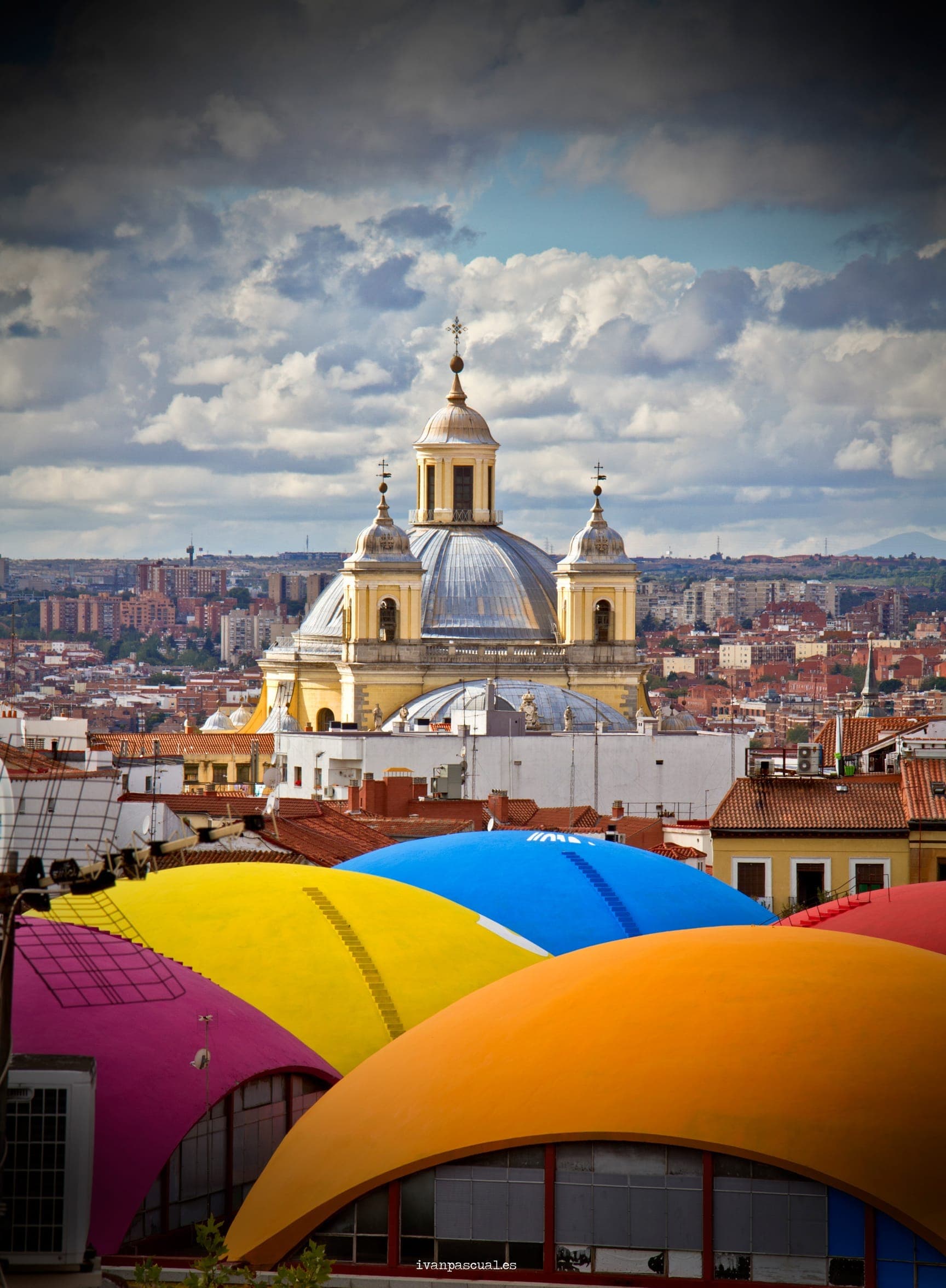 วิวของย่าน La Latina ในมาดริดที่มีมหาวิหาร San Francisco el Grande ทรงโดมและหลังคาตลาดหลากสีสันภายใต้ท้องฟ้ามีเมฆครึ้มอย่างน่าตื่นตา