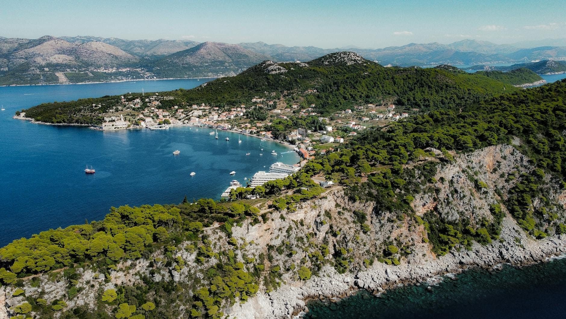 Luftaufnahme der Halbinsel Lapad mit üppig grünen Hügeln, klarem blauem Meer, kleinen Booten und einer entspannten Küstensiedlung in Kroatien.