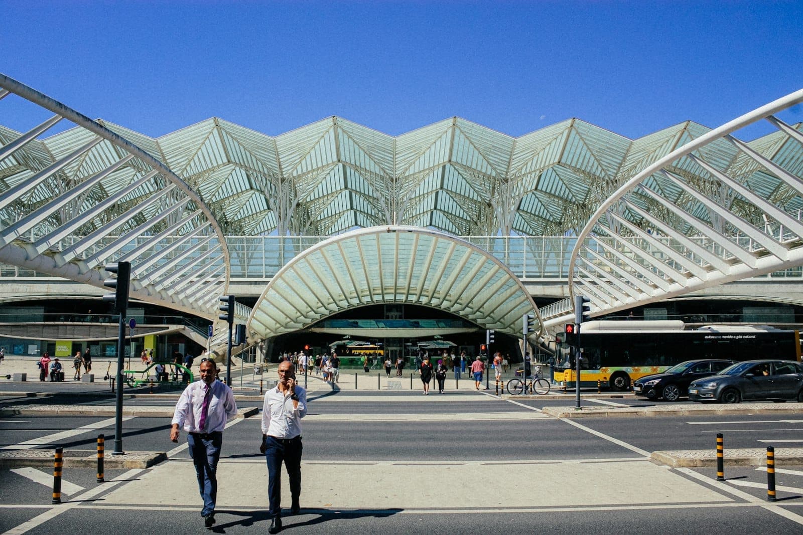 Exterior moderno da estação de transporte Lisboa Oriente com autocarros, pedestres e impressionante arquitetura de vidro e aço sob um céu azul.