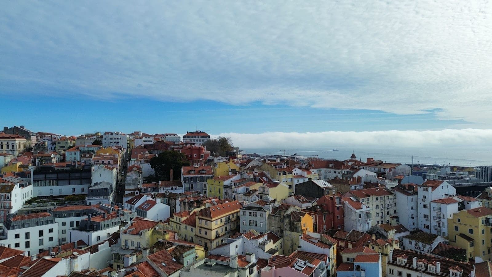 Paisagem urbana de Lisboa com casas em tons pastel e céu parcialmente nublado no inverno, a luz do dia revelando o carácter ameno e luminoso do clima de inverno.
