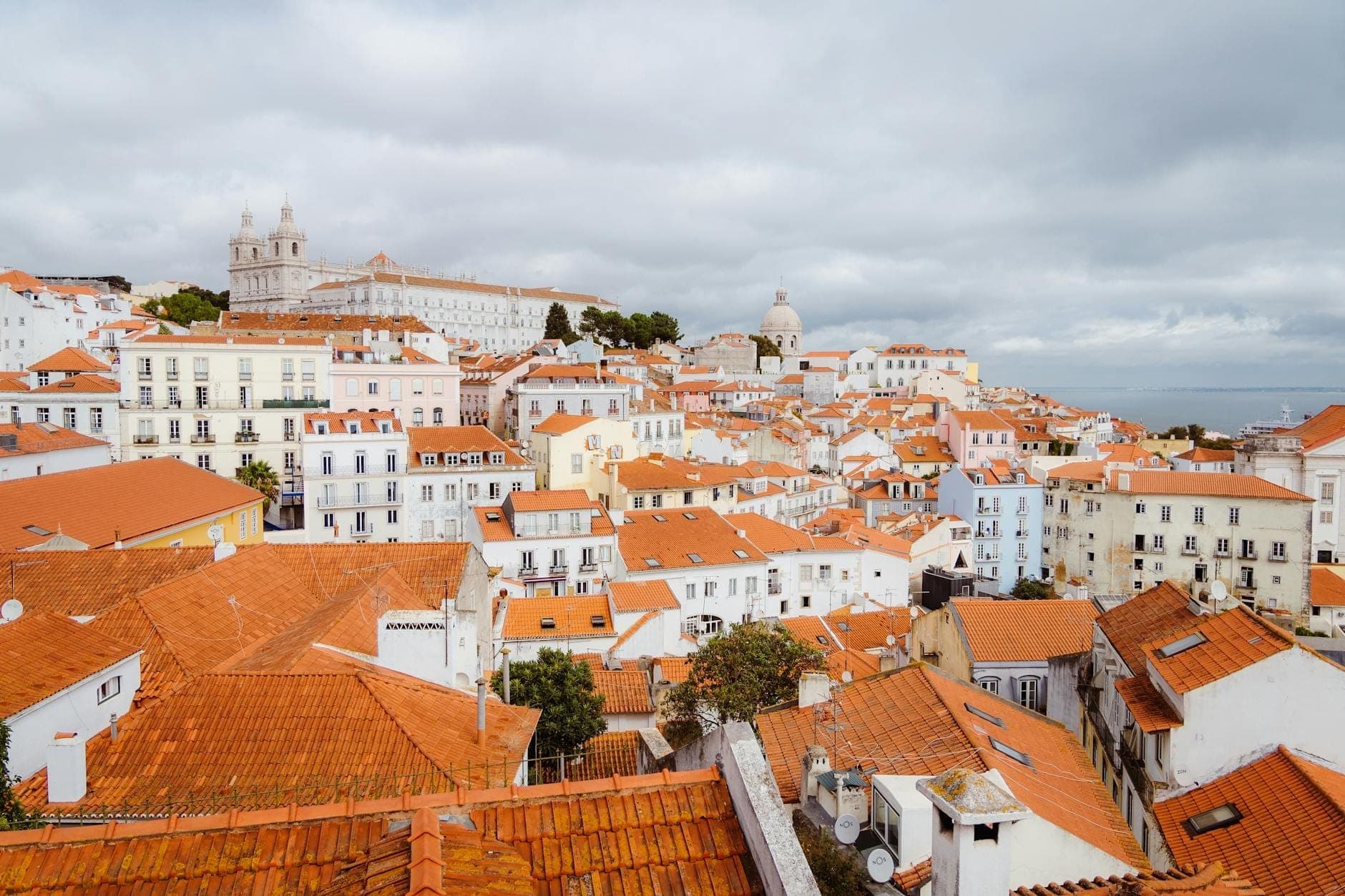 Vista panorâmica do bairro de Alfama em Lisboa com telhados vermelhos, edifícios históricos e céu nublado de inverno.