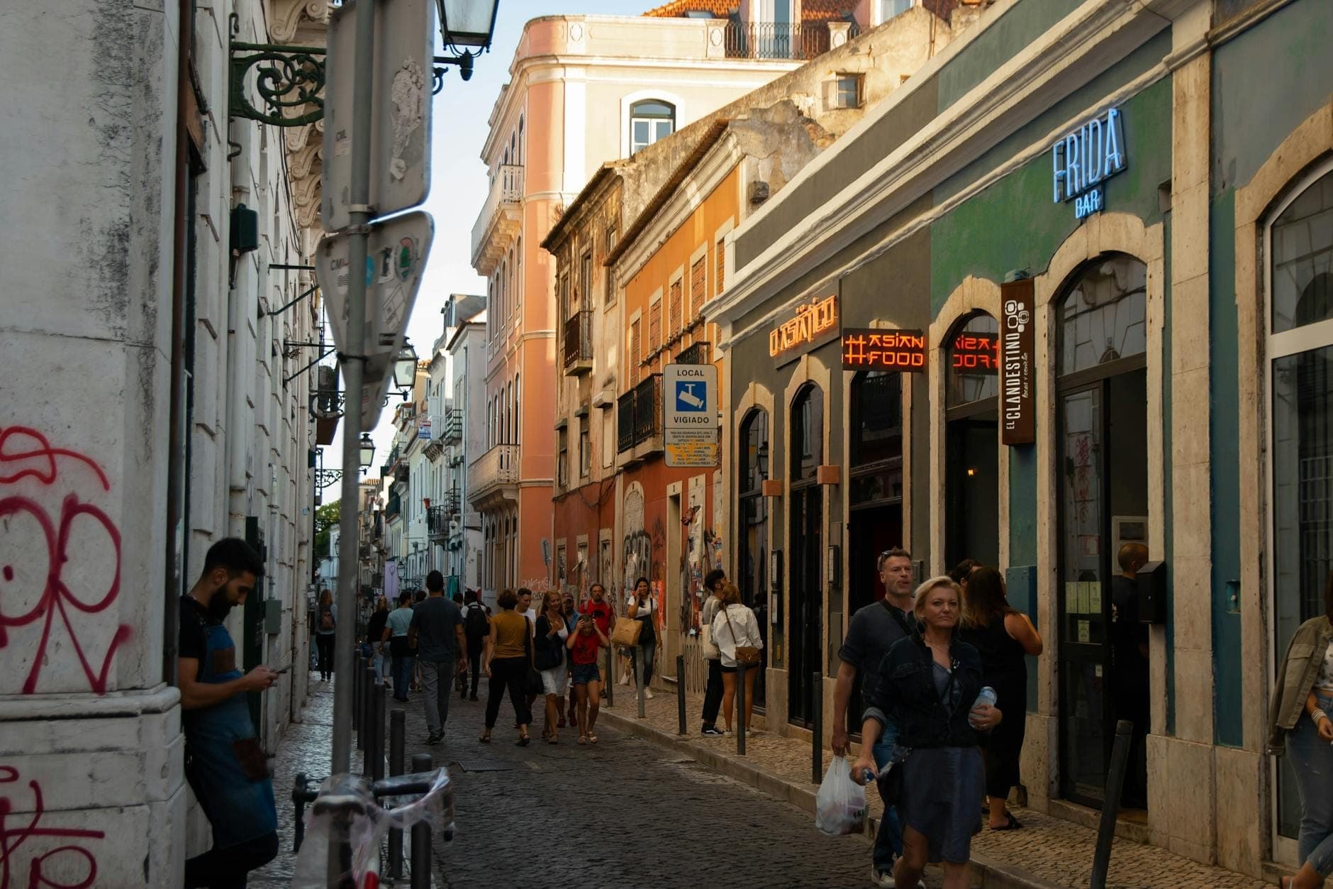 Rua estreita no Bairro Alto, Lisboa, repleta de bares e pessoas a caminhar e a conviver durante a noite.